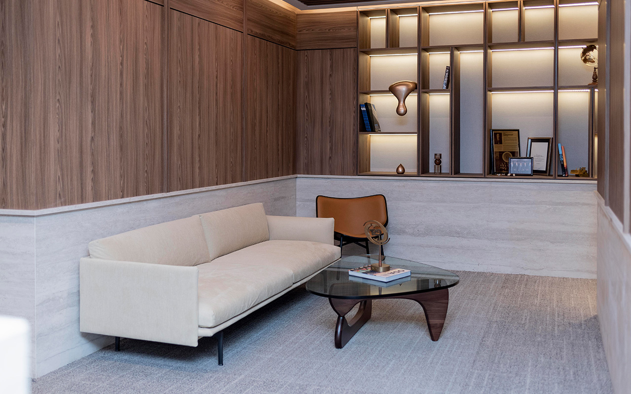 Sala con sofá beige, mesa de cristal y repisas iluminadas en muro de madera.