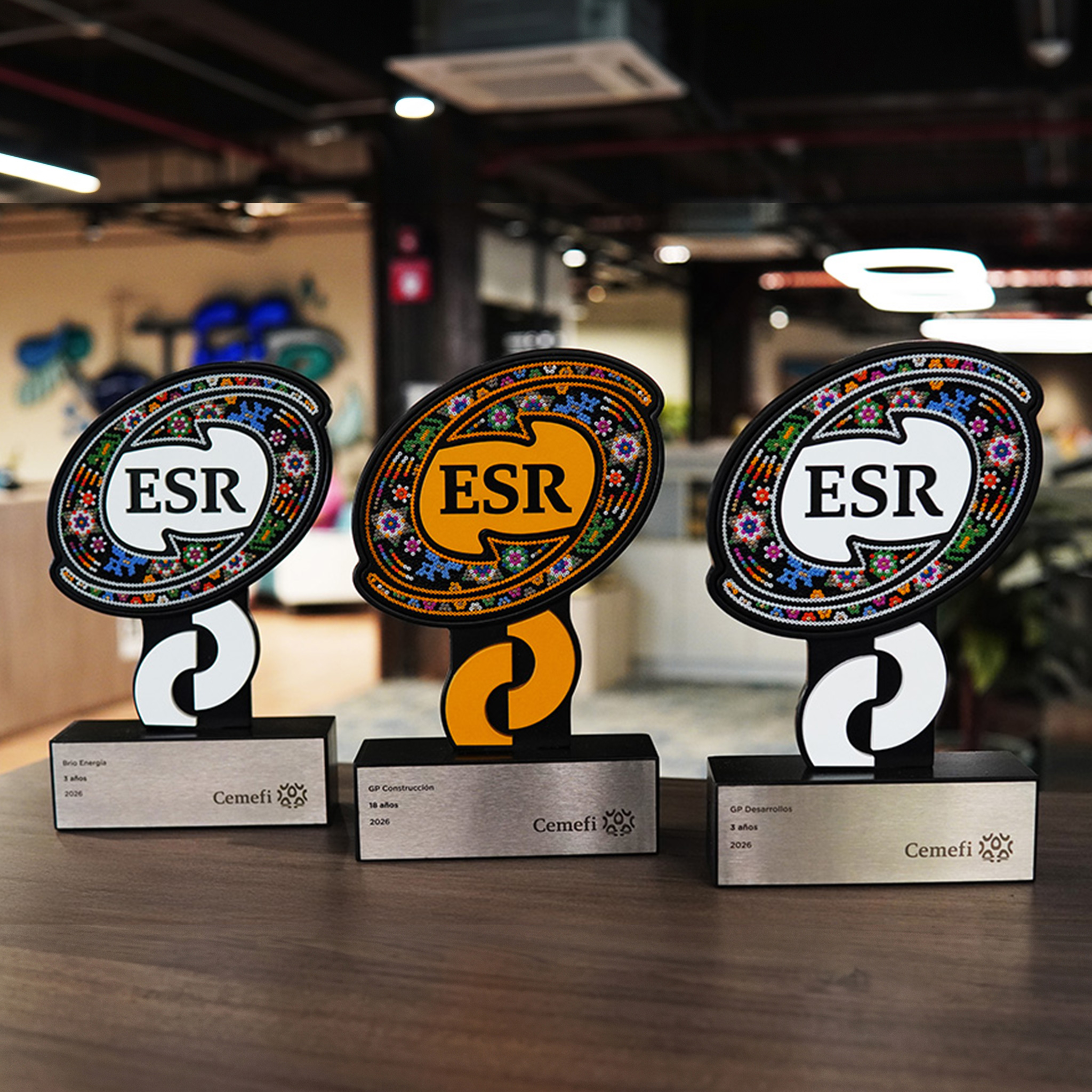 Three Cemefi ESR trophies on a wooden table, with the office in the background.