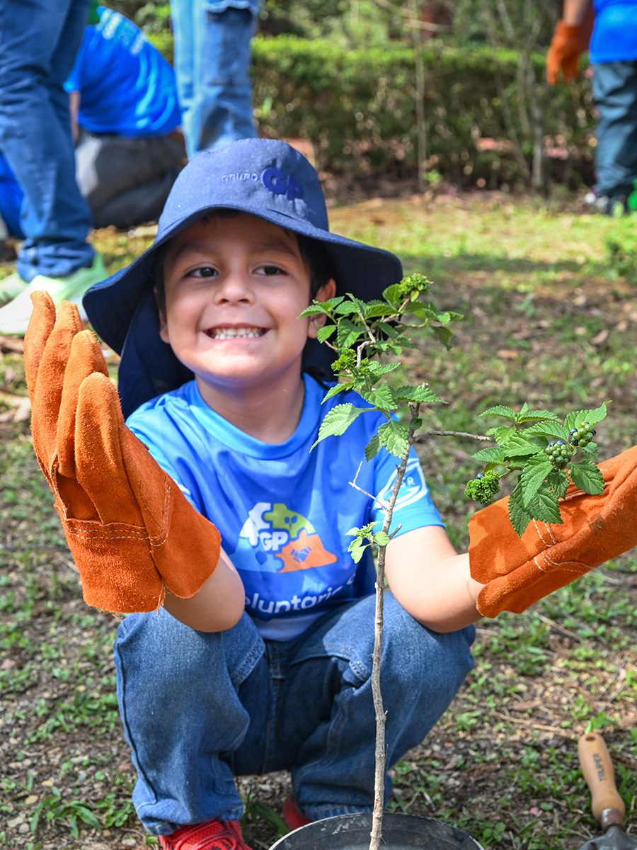A boy wearing gloves and a Grupo GP cap is holding a newly planted sapling.