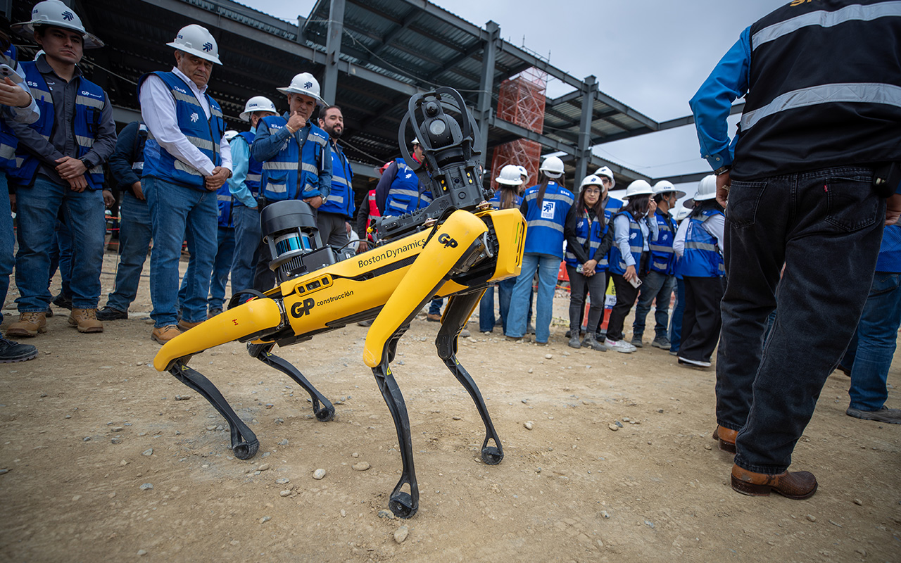 Robot cuadrúpedo amarillo de GP camina en la obra, rodeado de personal con casco.