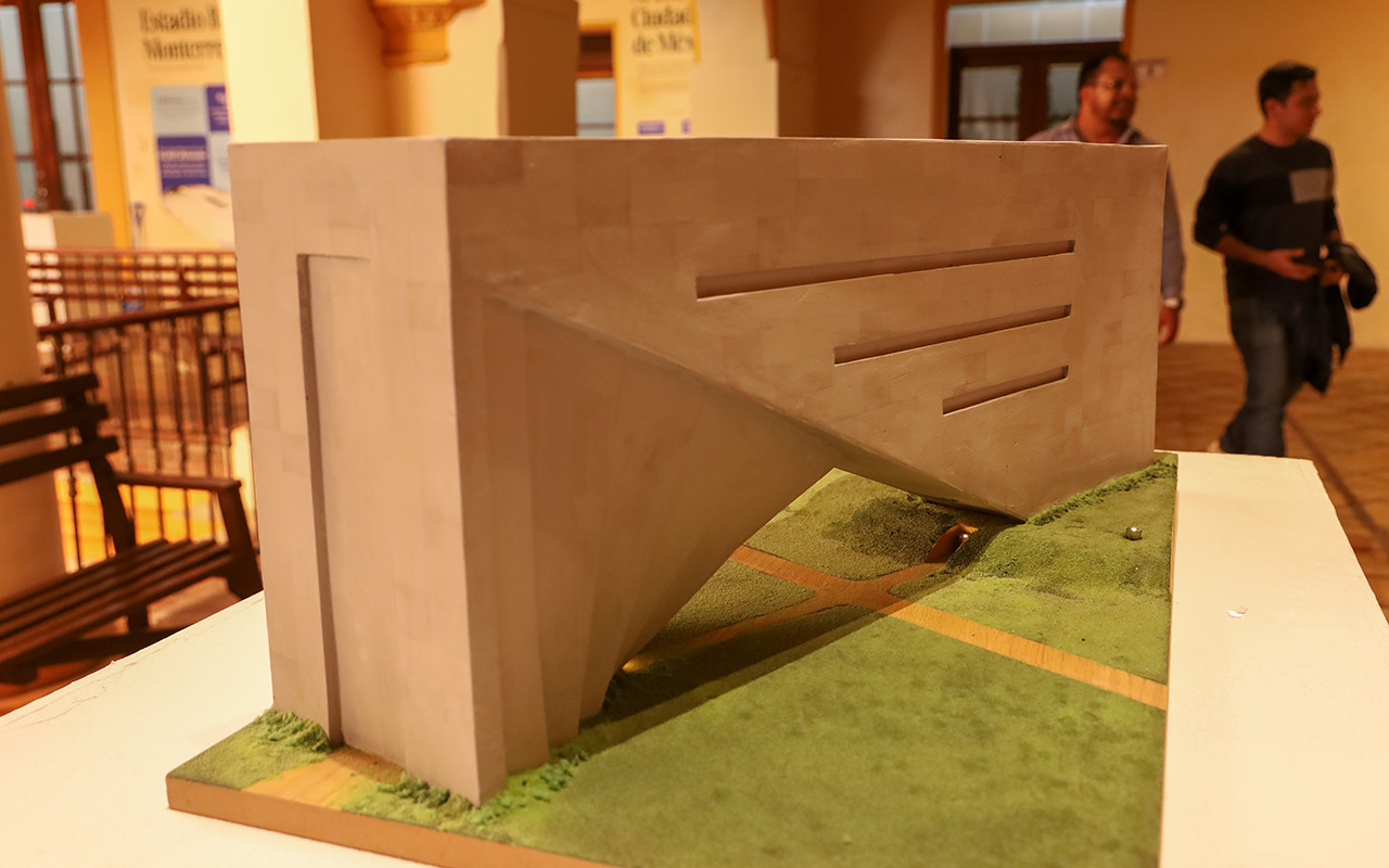 Maqueta de concreto de un volumen en voladizo, exhibida sobre una base verde.