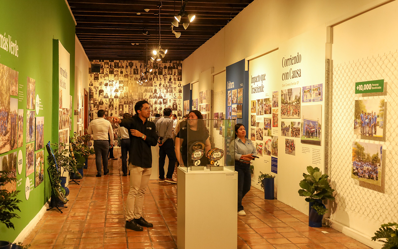 Visitantes recorren la sala con muro de retratos, trofeos y Corriendo con Causa.