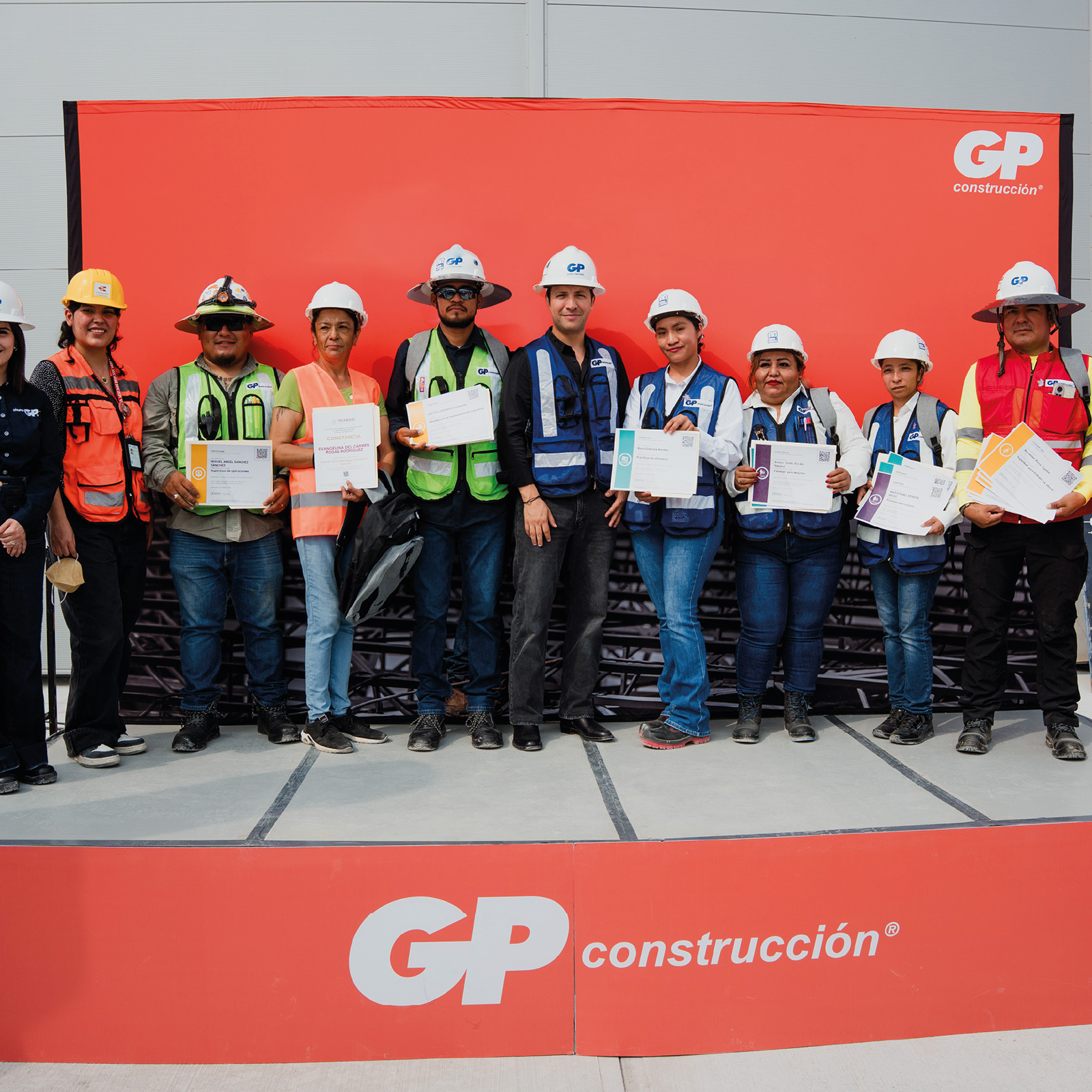 Grupo con cascos y chalecos sostiene constancias en el escenario de GP Construcción.