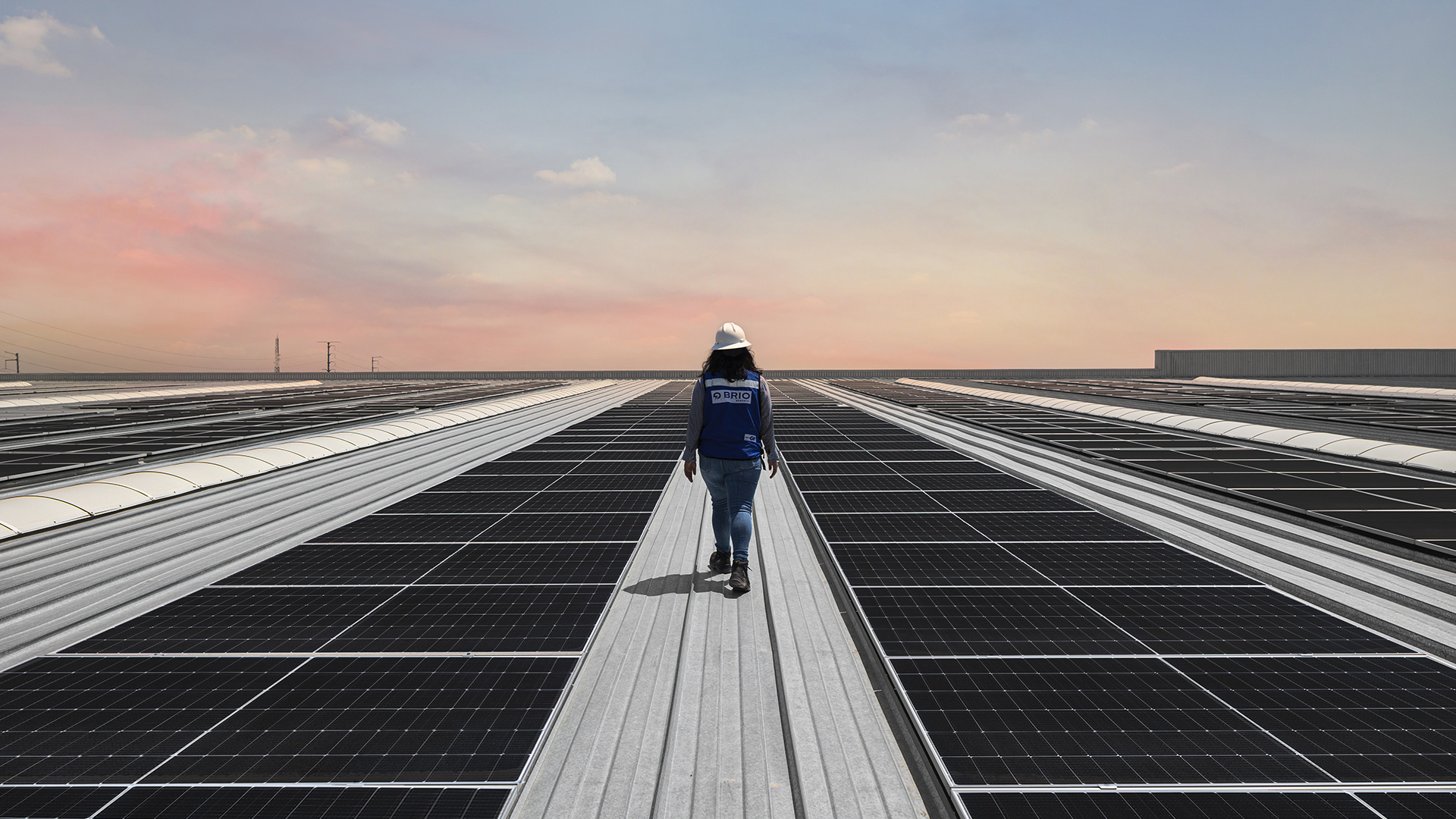 Persona con chaleco azul camina entre filas de paneles solares en una azotea.