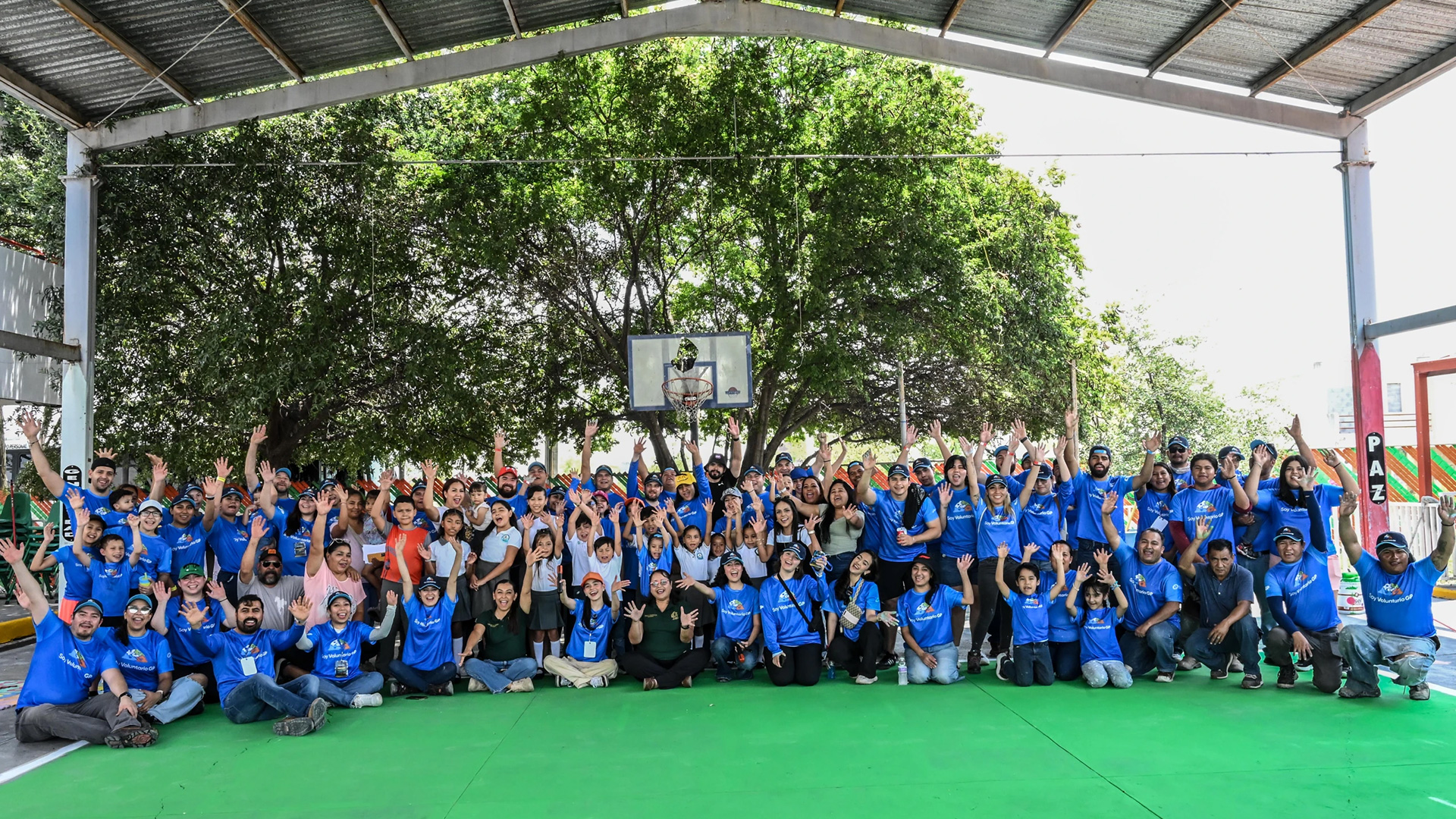 Voluntariado de Grupo GP reunido bajo un techo, con las manos en alto, en una cancha.