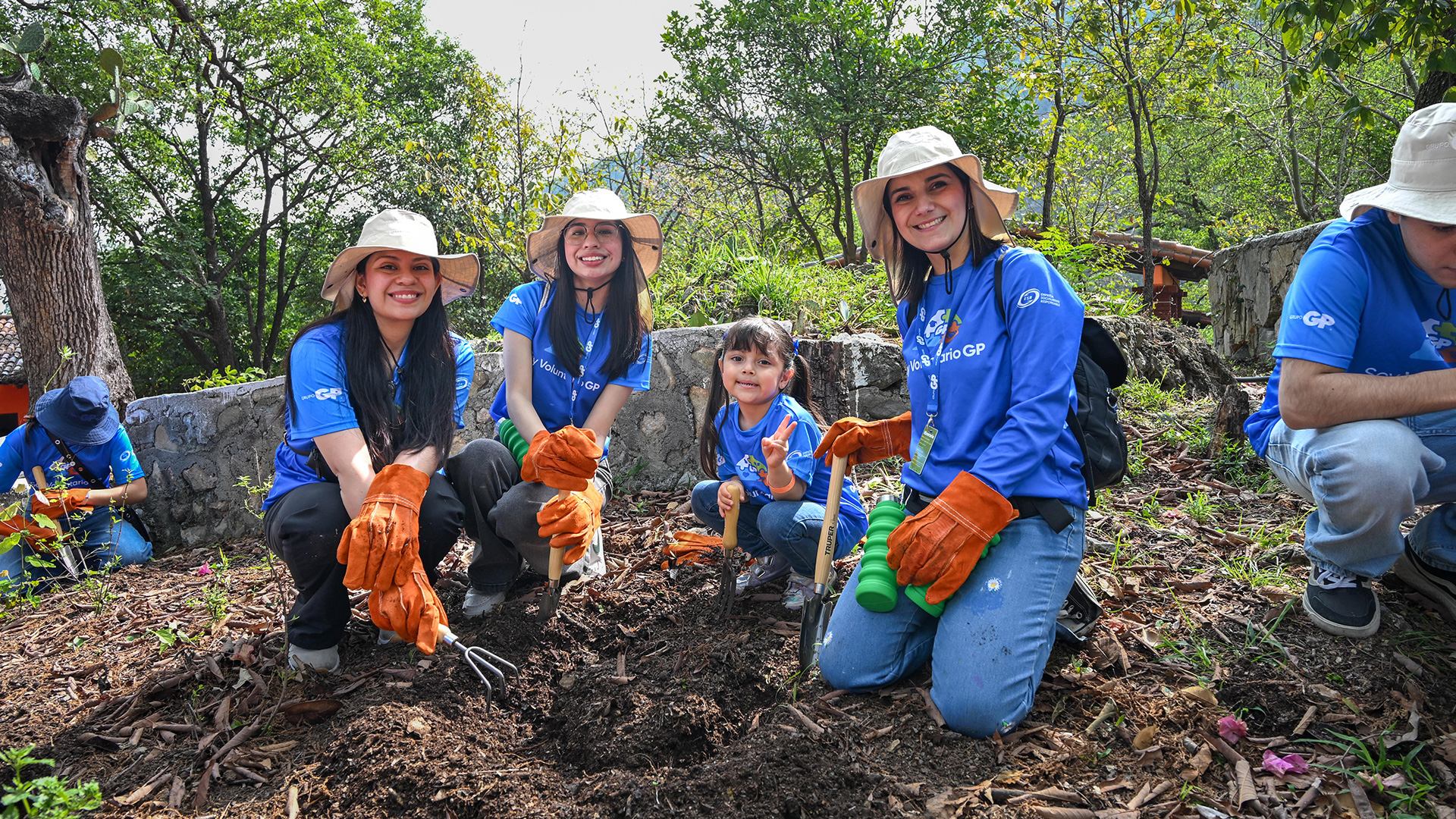 Grupo de voluntarios con sombrero planta en un talud arbolado, con herramientas en mano.