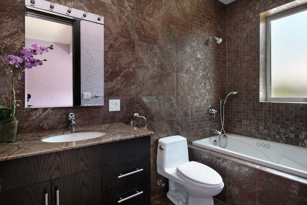 Modern bathroom with stone-look tile walls, vanity mirror, and bathtub