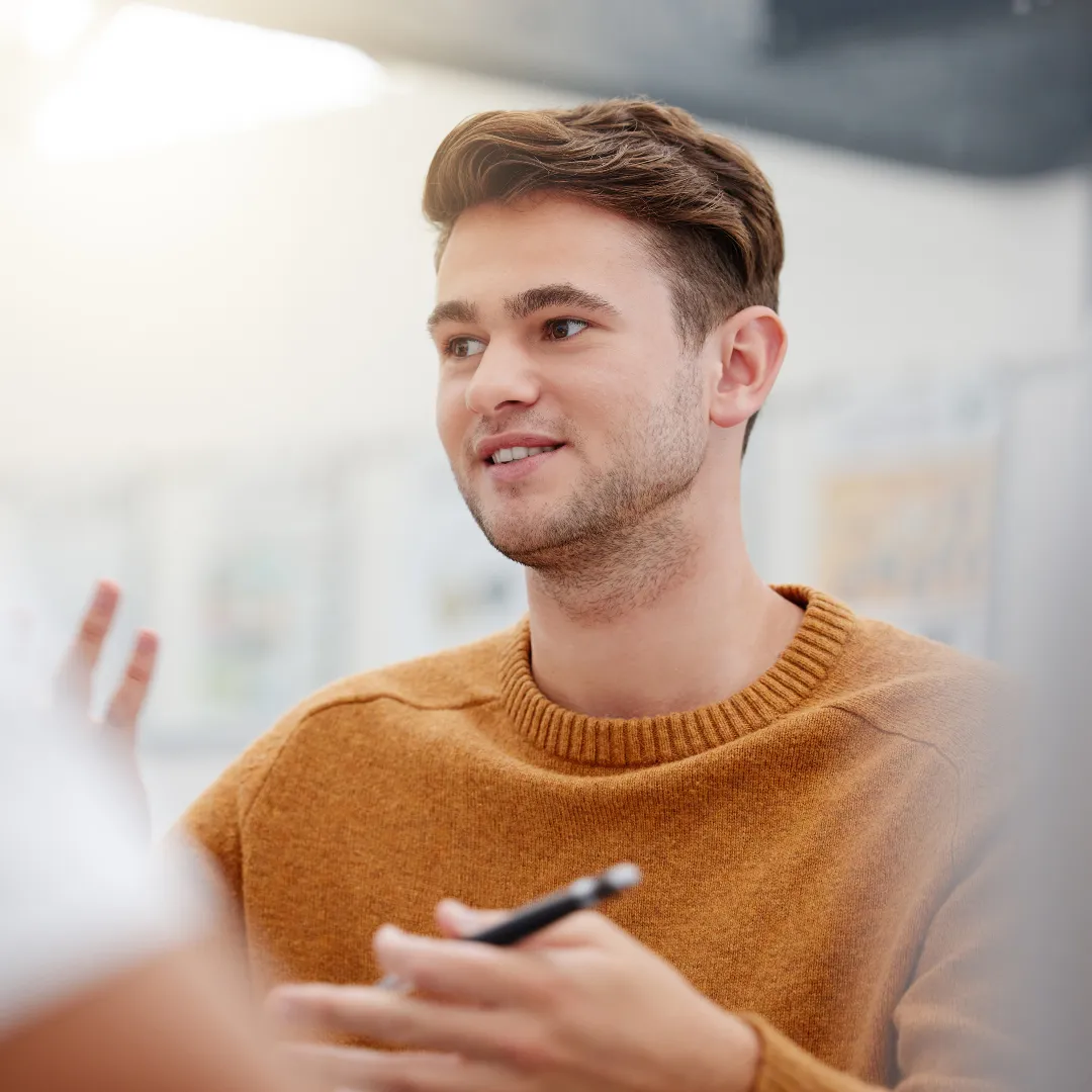 Accountant in a brown sweater smiling and gesturing while holding a pen during a conversation.
