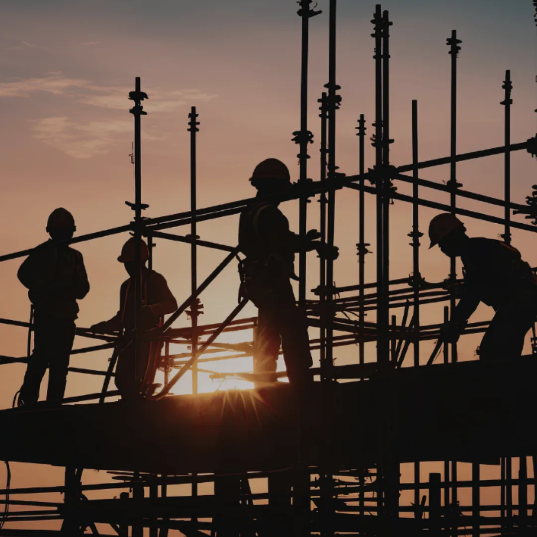 Construction workers wearing helmets on scaffolding at sunset.