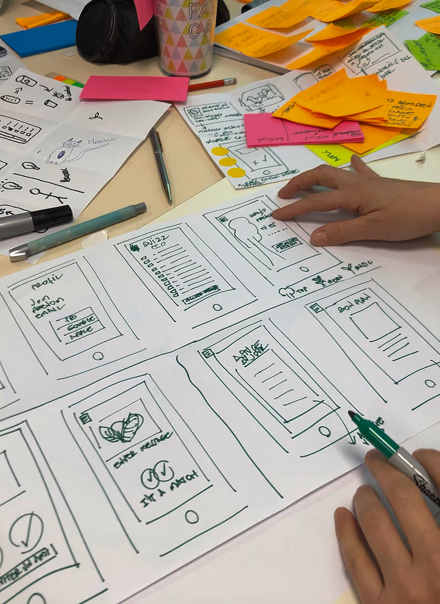 Hands sketching mobile app wireframes on paper with sticky notes and markers on a desk.