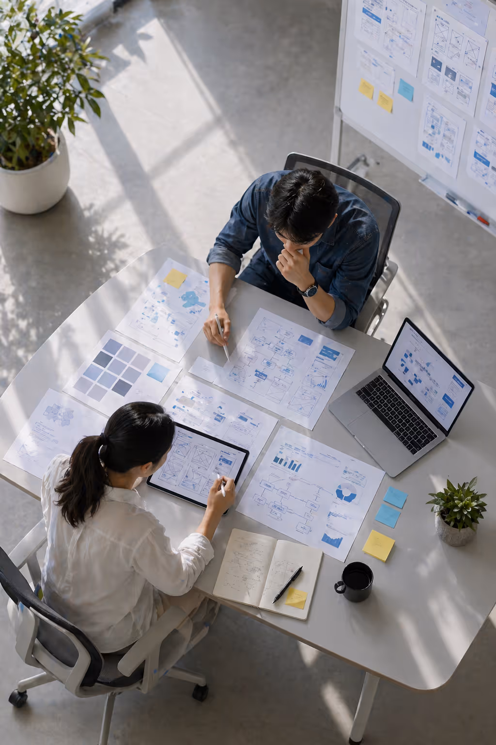 Two coworkers reviewing charts and wireframes on paper and digital devices at a well-lit office table.