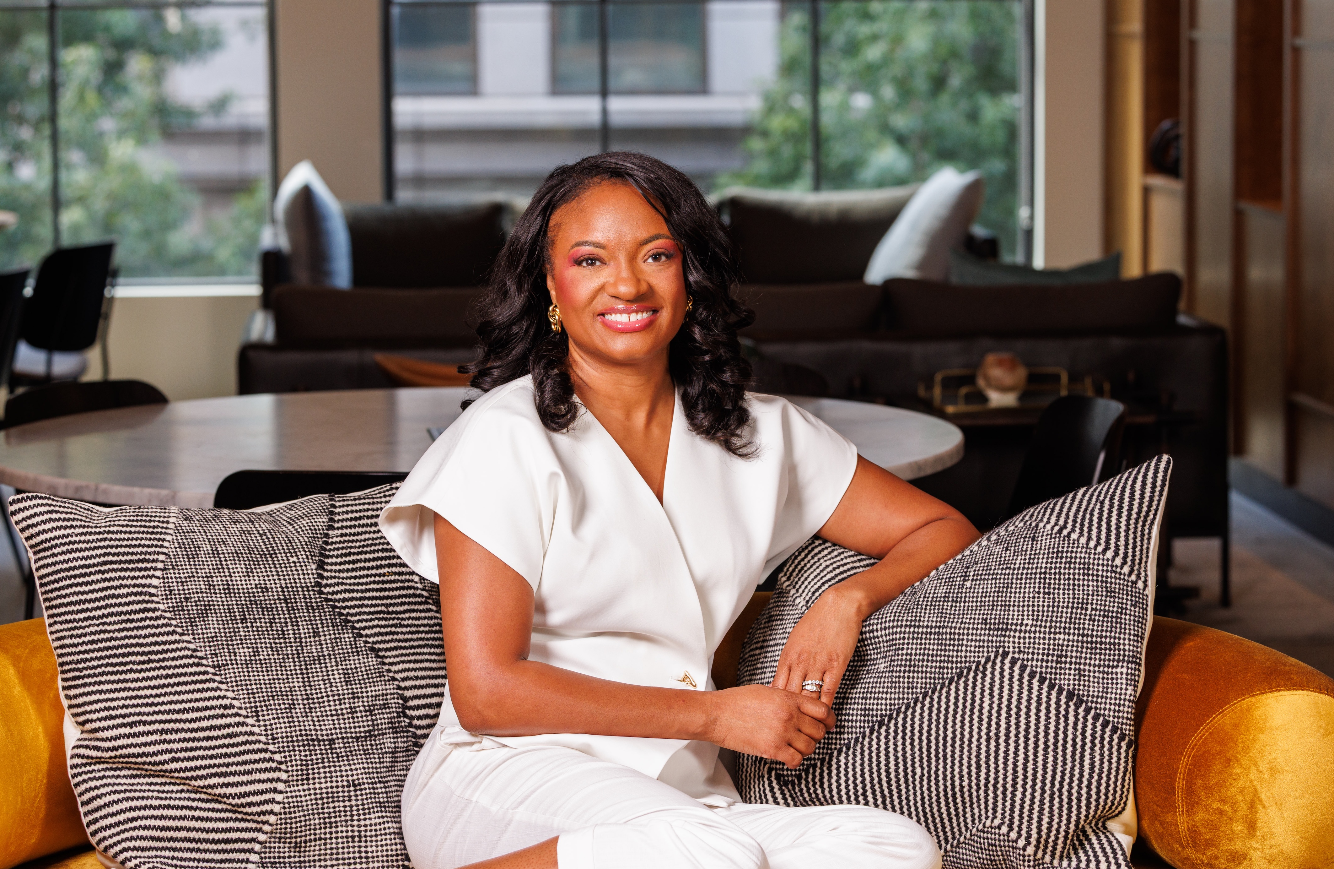 Shavonn Richardson, Founder and CEO of Think and Ink Grant Consulting, seated on a gold sofa in a professional setting wearing white