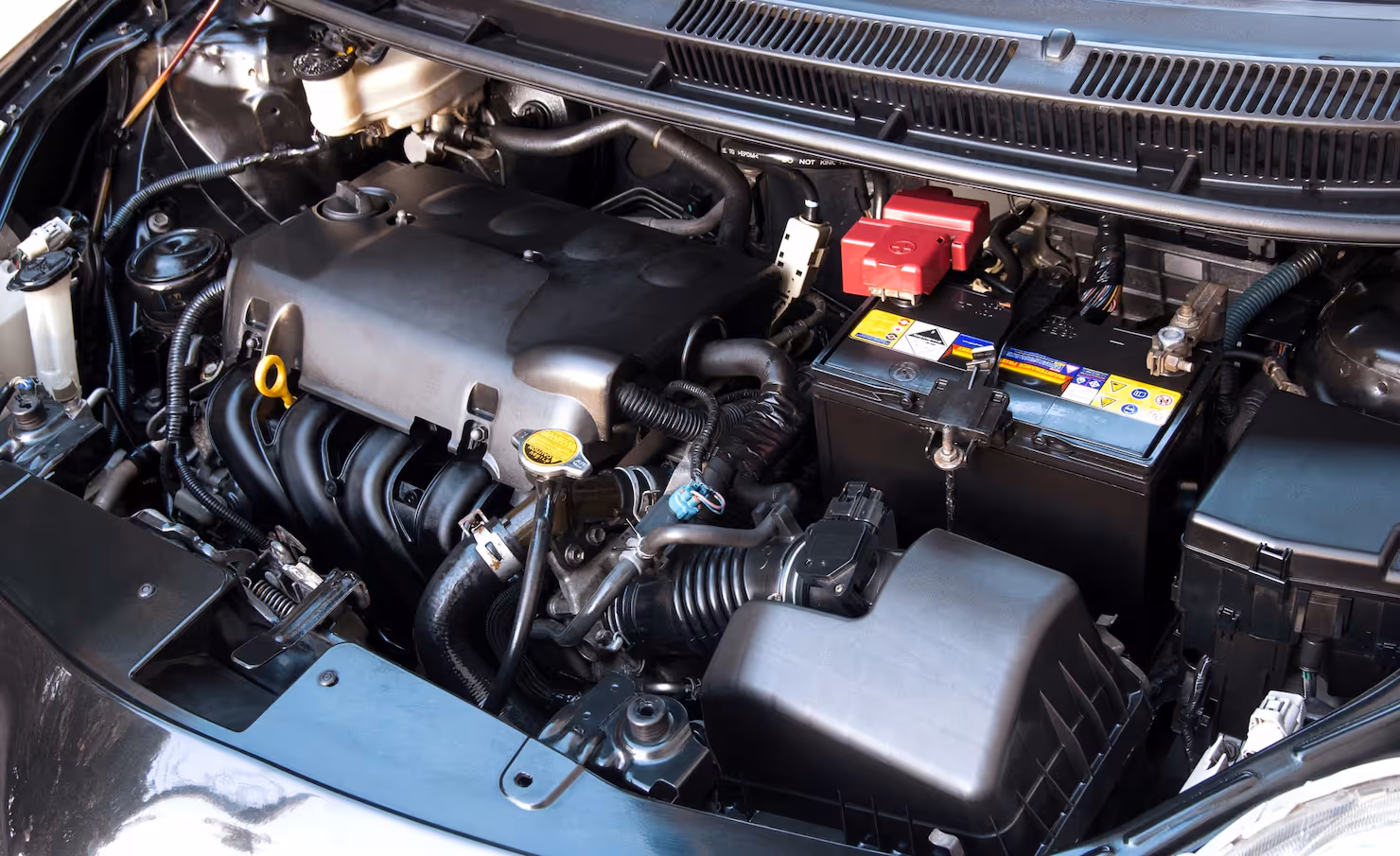 Clean car engine bay showing battery, air filter housing, and various engine components with plastic covers and hoses.
