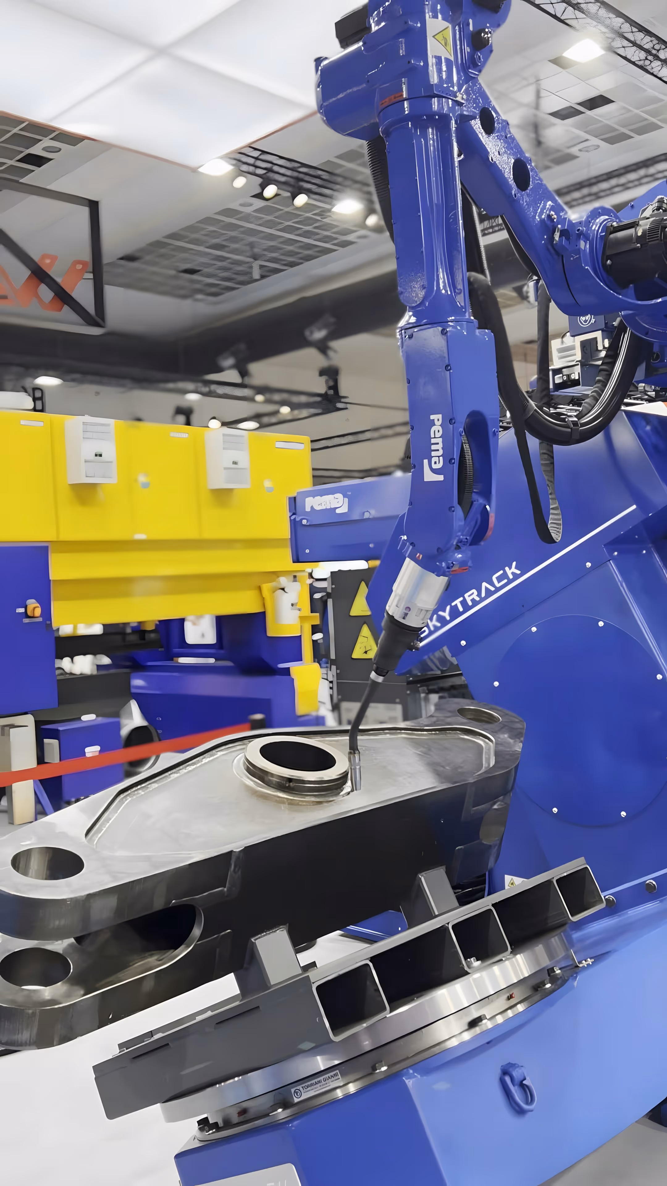 Blue industrial robotic arm labeled Skytrack working on a metal component in a manufacturing facility.