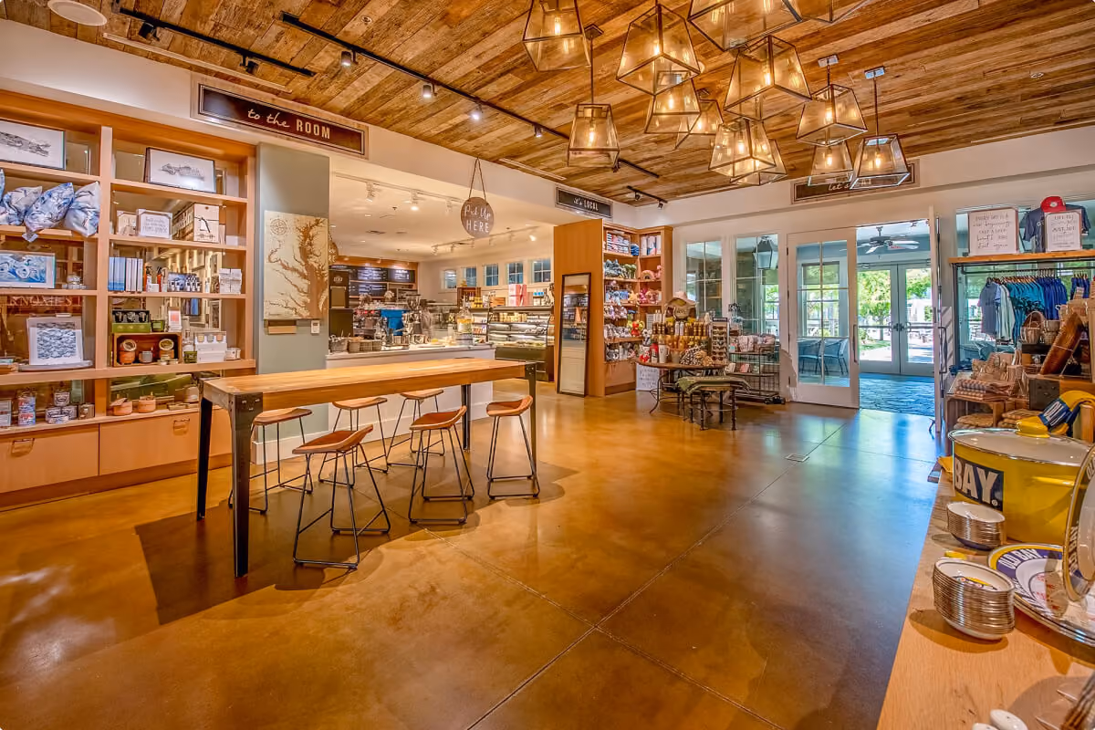 Interior of a cozy market featuring wooden furniture, hanging pendant lights, shelves with various goods, and a café counter in the background.