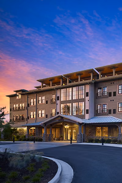 Exterior of a modern multi-story building with large windows at sunset under a colorful sky.