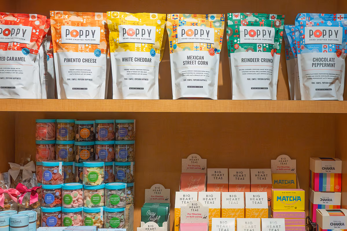 Shelf displaying colorful bags of Poppy hand-crafted popcorn flavors and assorted candy jars and tea boxes.