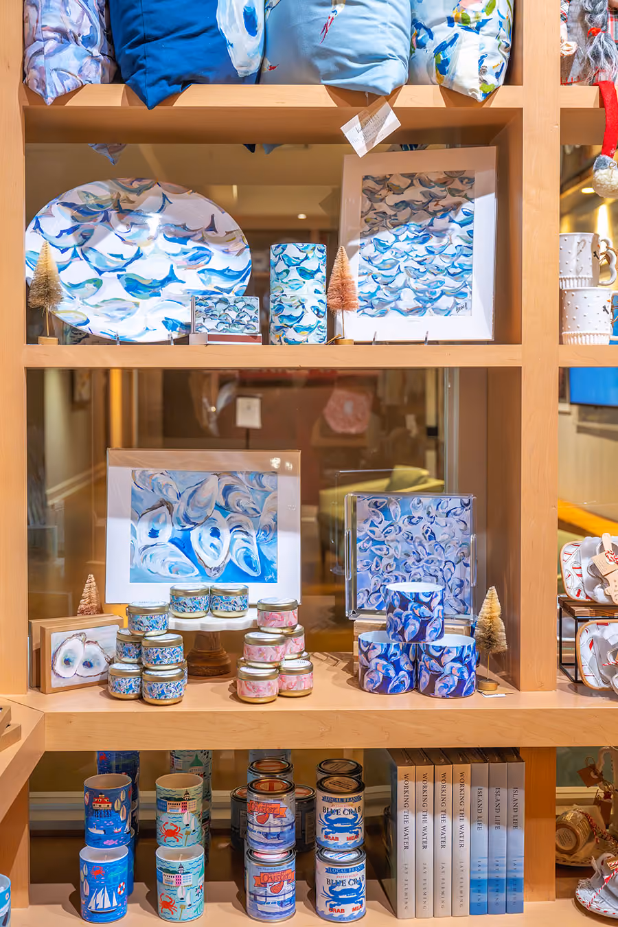 Wooden shelf displaying decorative items including blue and white pottery with shell and ocean motifs, candles, framed artwork, and coffee mugs.