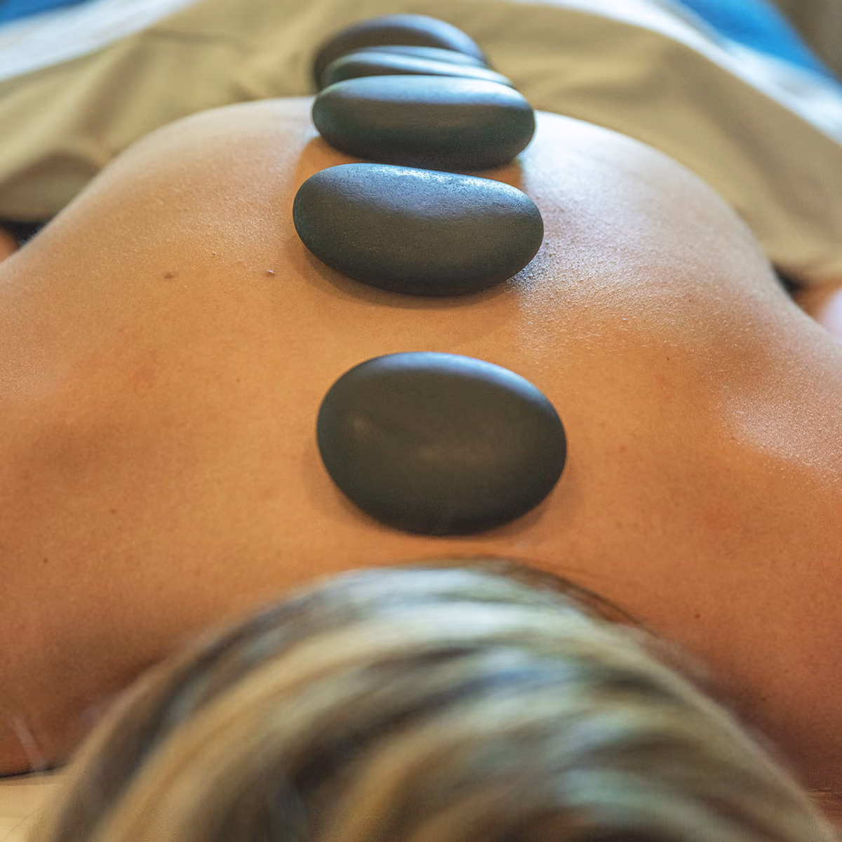 Four smooth black hot stones placed on a person’s bare back during a spa massage.