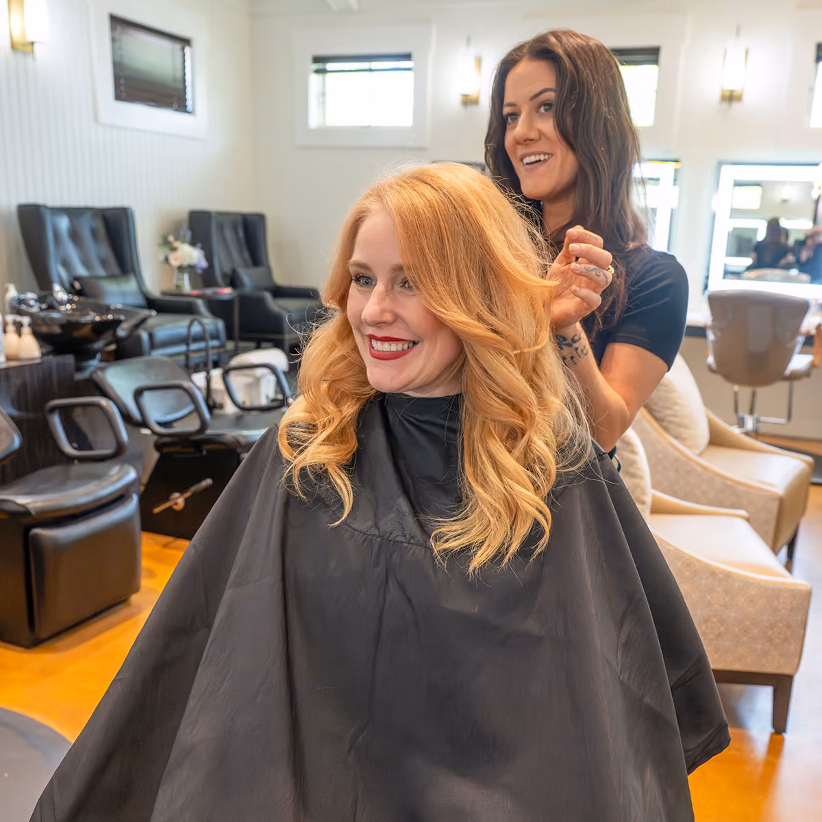 Hairdresser styling blonde woman's long wavy hair in a bright salon.