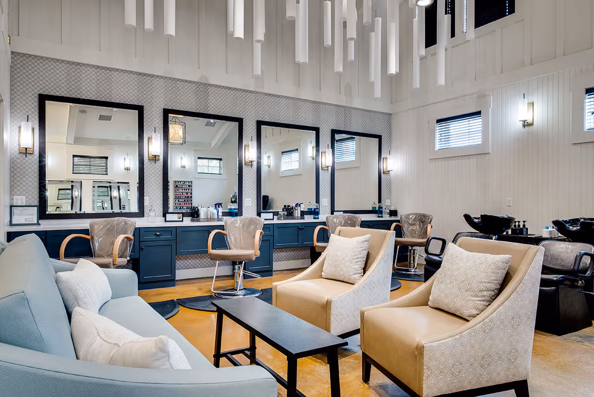 Modern salon area with blue styling stations, brown chairs, beige armchairs with cushions, a blue couch, and large mirrors.
