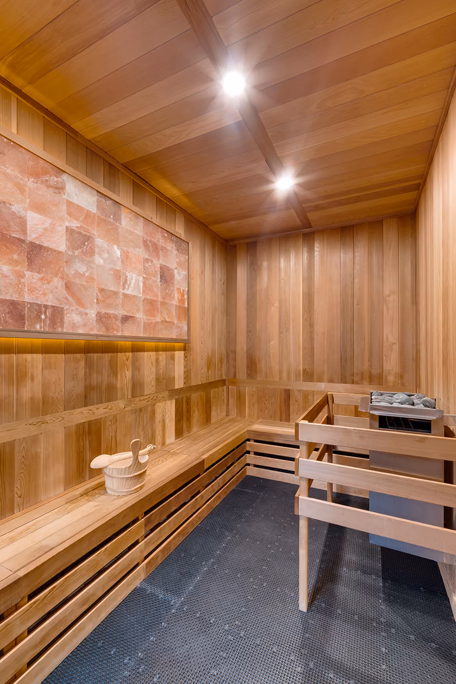 Interior of a wooden sauna with benches, a bucket with ladles, and a heater with stones.
