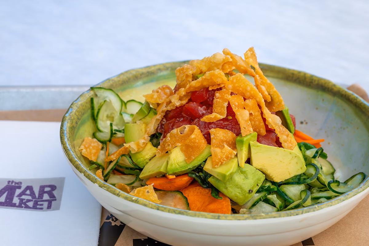 A bowl of poke with raw fish, avocado, cucumber, carrots, greens, and crispy wonton strips.