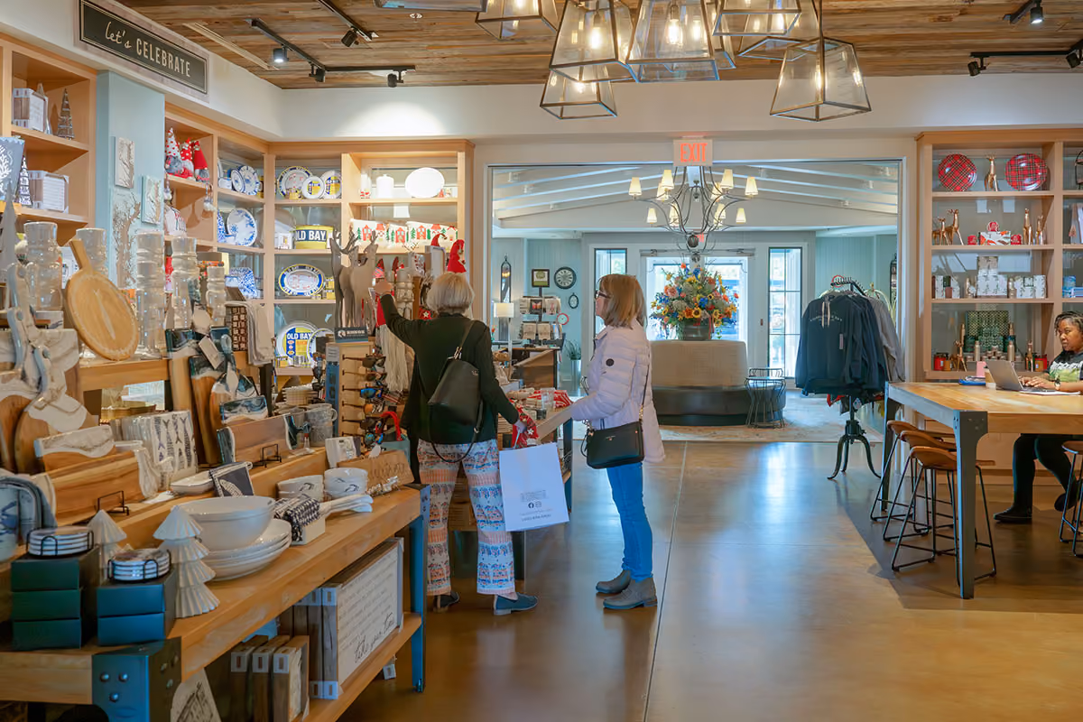 Two women shop in a well-lit gift store filled with ceramics, kitchenware, and decorative items.