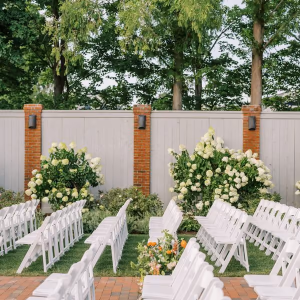 Outdoor garden wedding ceremony setup with white folding chairs and hydrangea florals