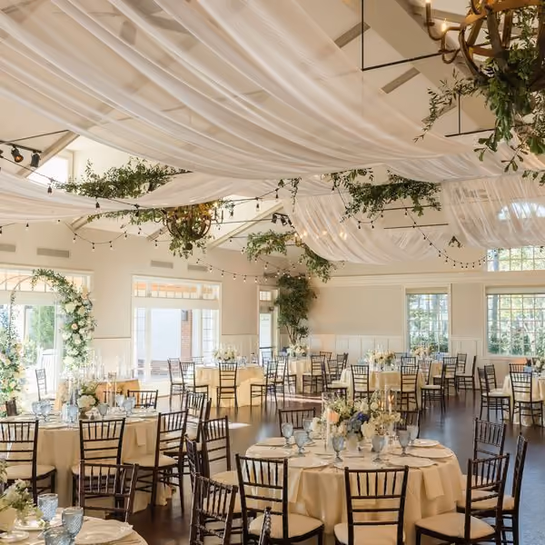 Wedding reception hall with a draped ceiling, greenery chandeliers and round tables