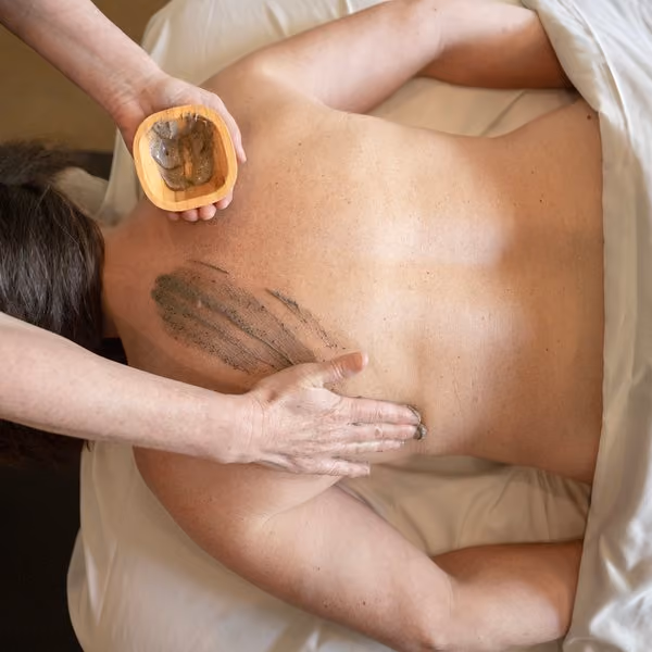 Therapist applying an exfoliating body scrub during a back treatment at The Spa