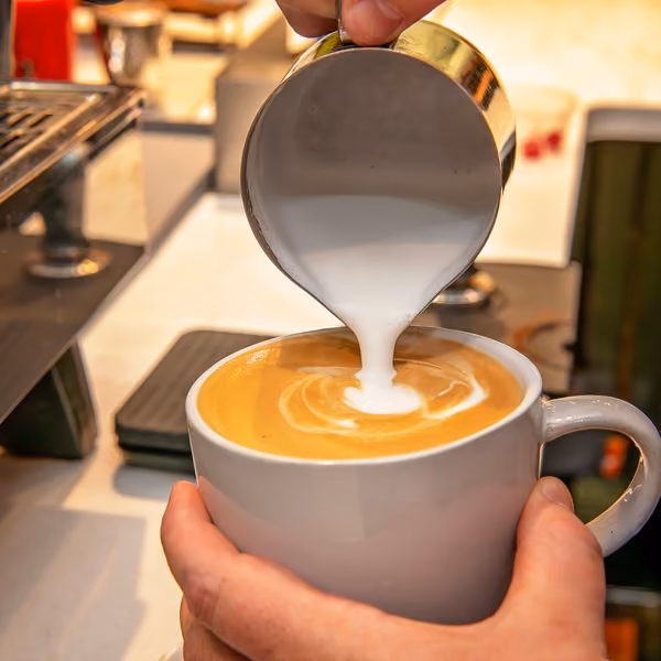 Barista pouring steamed milk into a latte at The Market