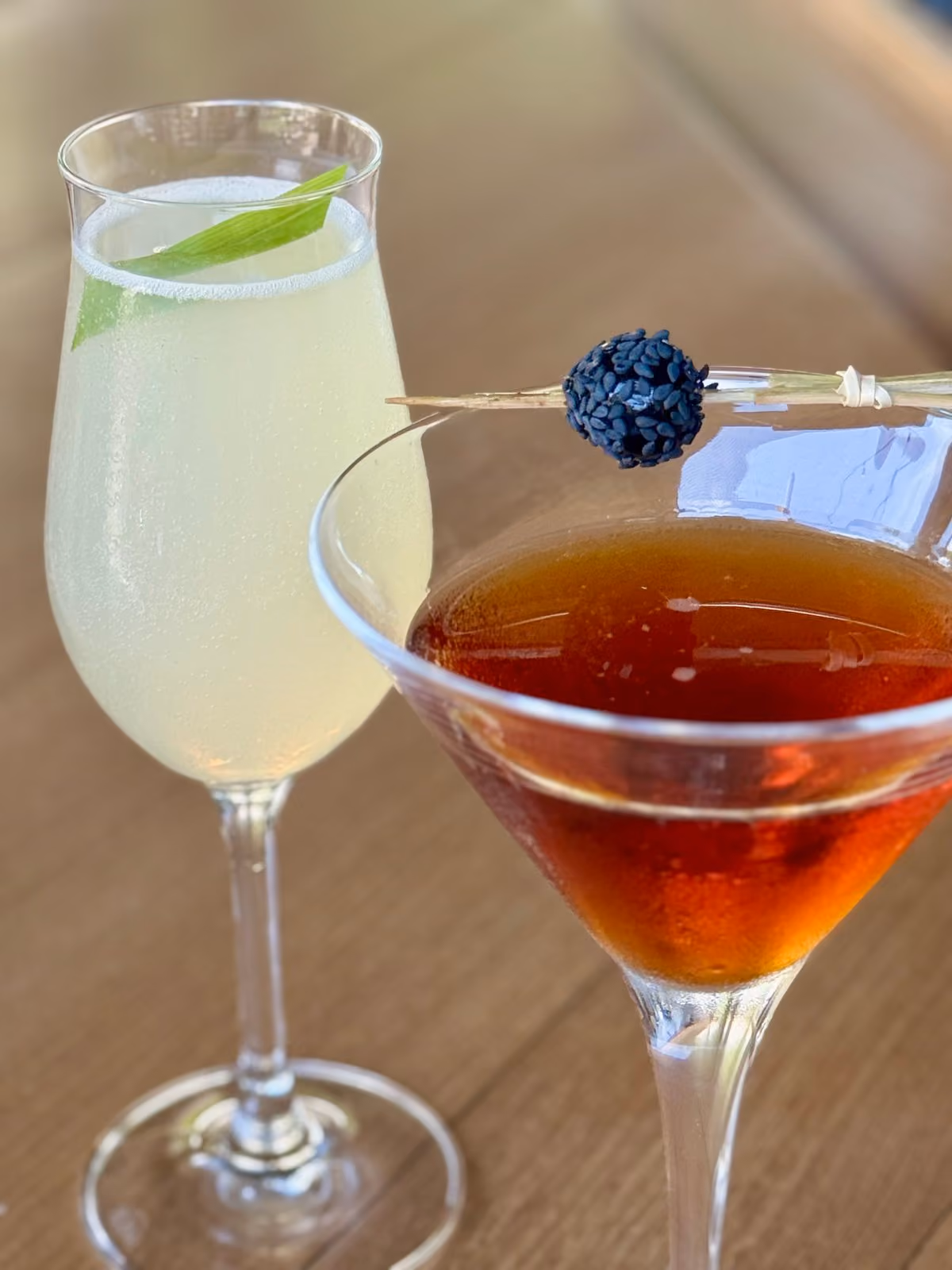 Two craft cocktails at Vue — a light yellow champagne-glass cocktail with basil and a dark amber martini with a blackberry garnish