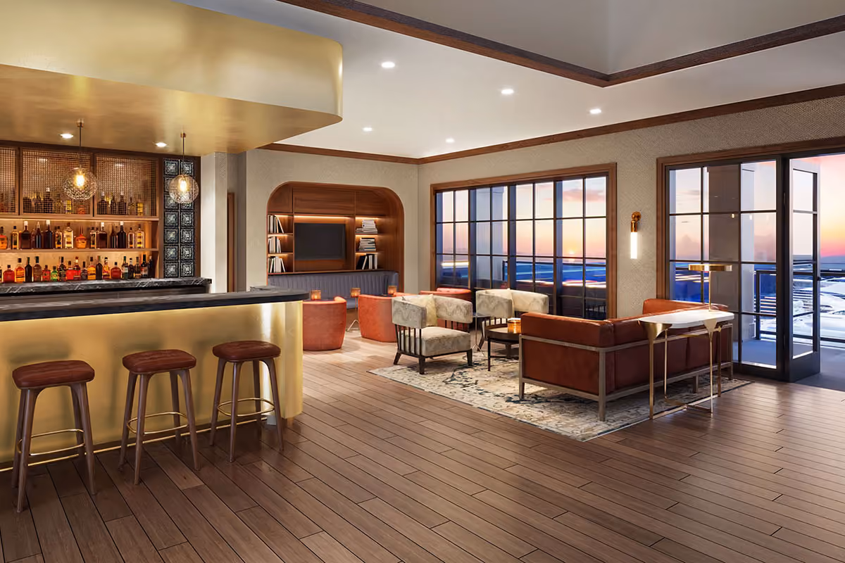 Modern lounge with a bar, leather seating, bookshelves, and large windows overlooking a sunset view.
