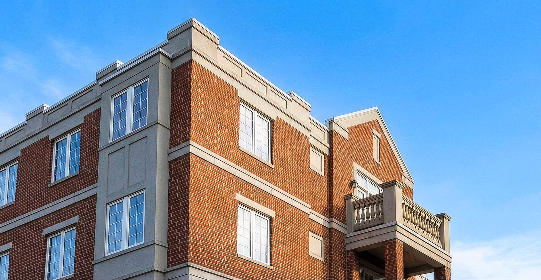 Corner view of a red brick and stone residential building under a clear blue sky.