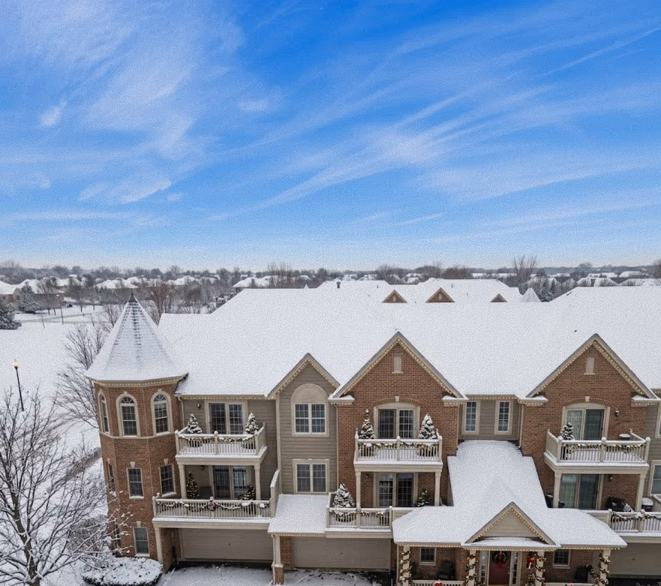 Snow-covered townhouse complex with balconies decorated for Christmas under a blue sky.