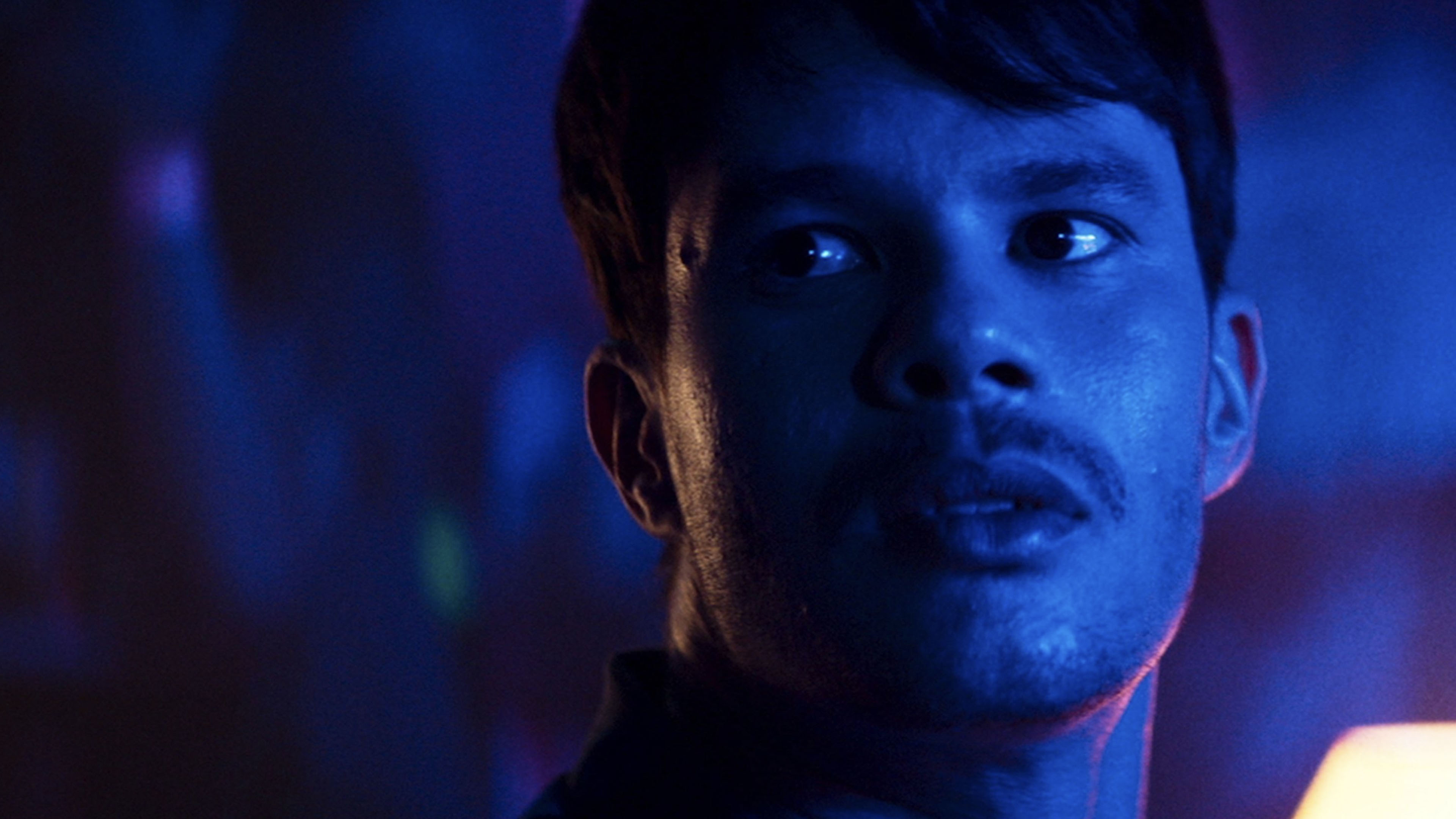 Close-up of a young man under blue neon lighting in a tense scene from the gay drama film The Best Friend