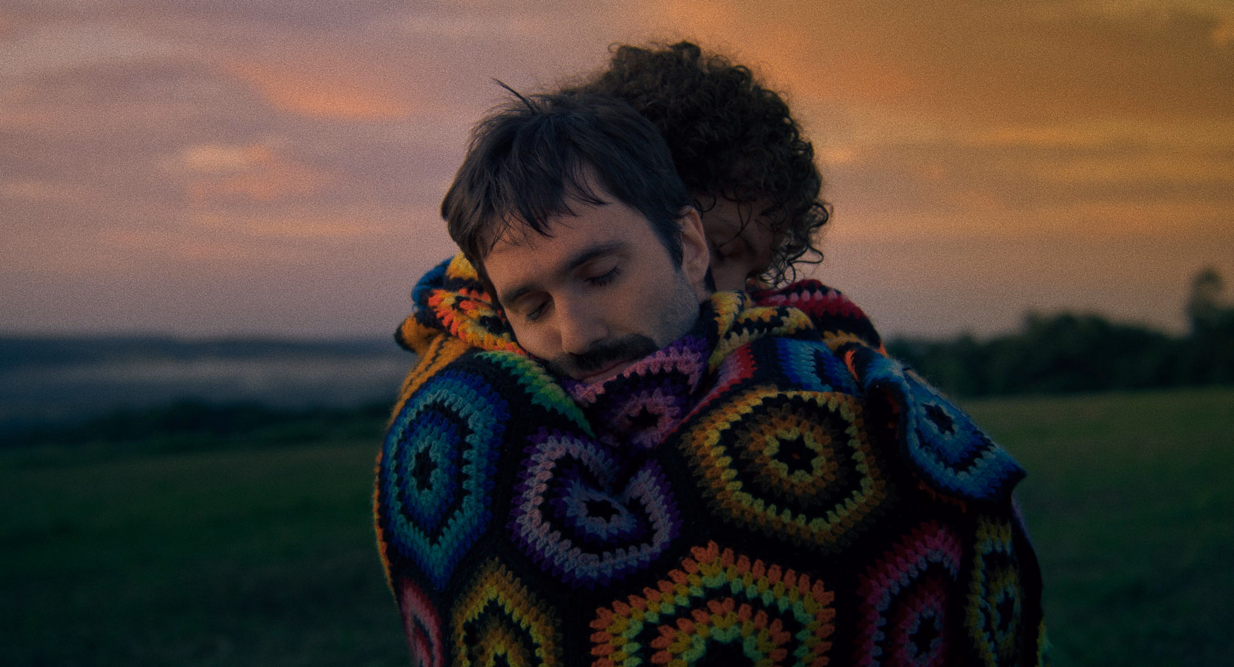 Two men embrace in a beutiful afghan blanket.