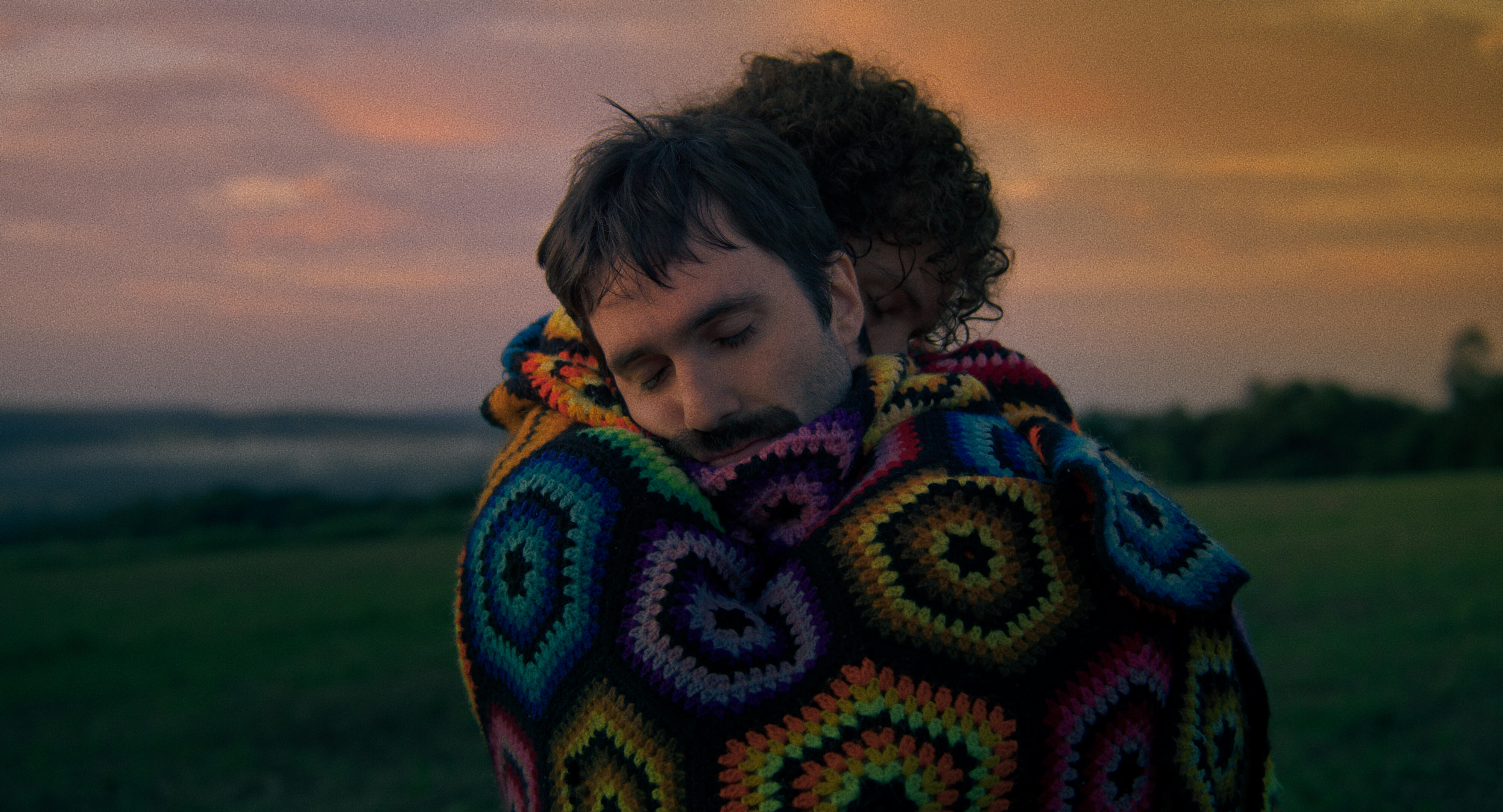 Two men embrace in a beutiful afghan blanket.