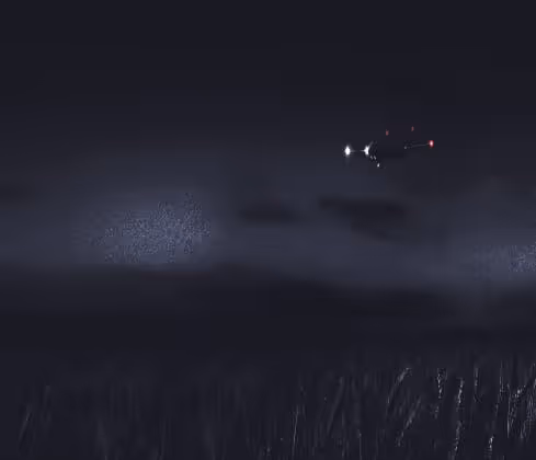 Drone flying at night with a bright front light illuminating falling rain over tall grass.