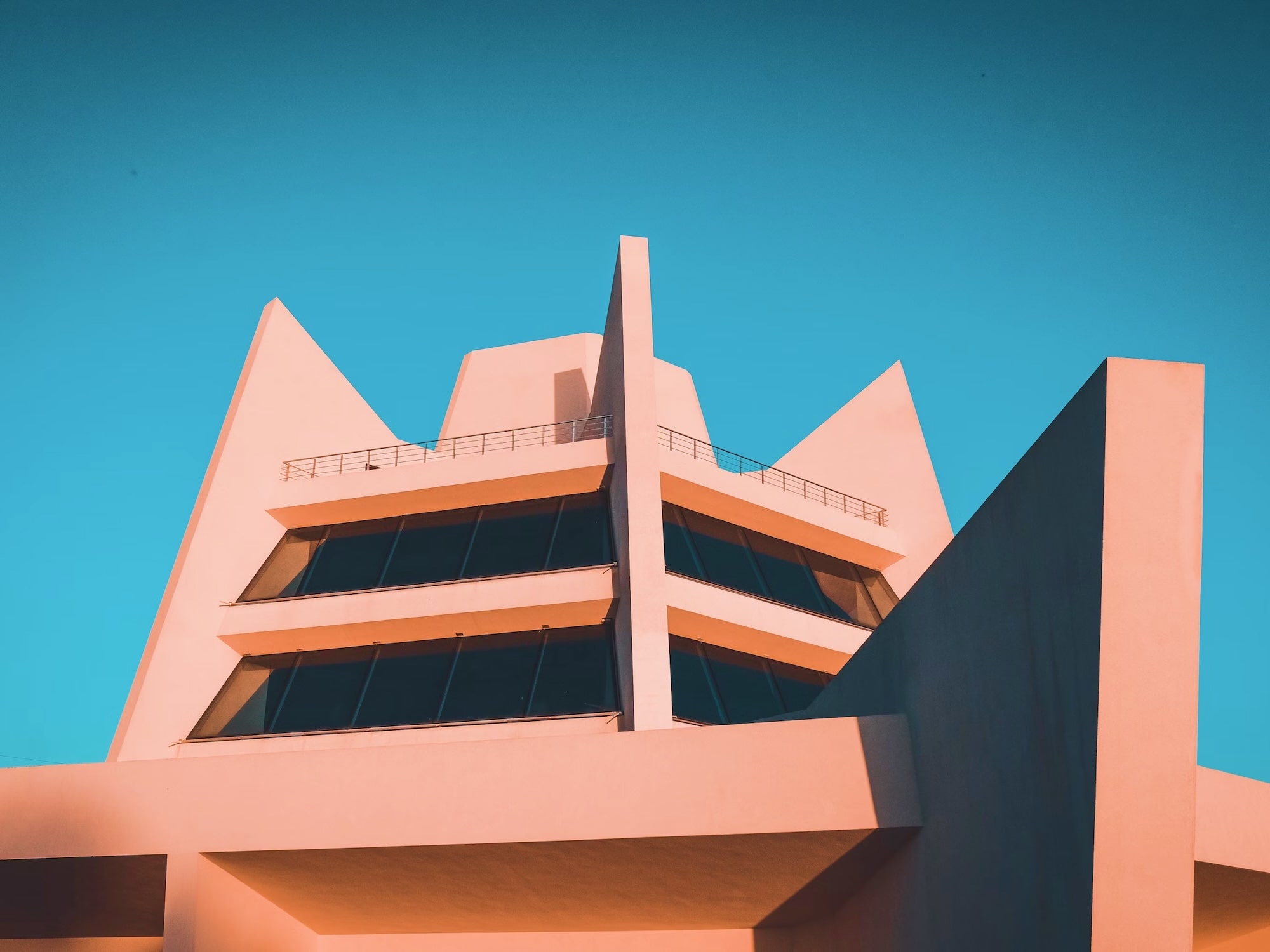 Modern building with sharp angular architectural design and large dark windows against a clear blue sky.