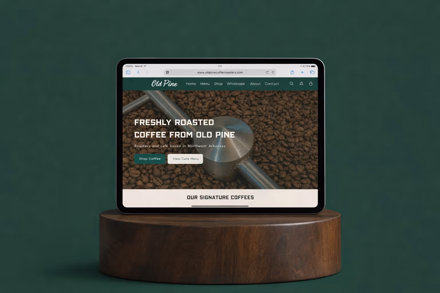 Tablet displaying Old Pine Coffee Roasters website homepage with coffee beans background, placed on a round wooden stand.