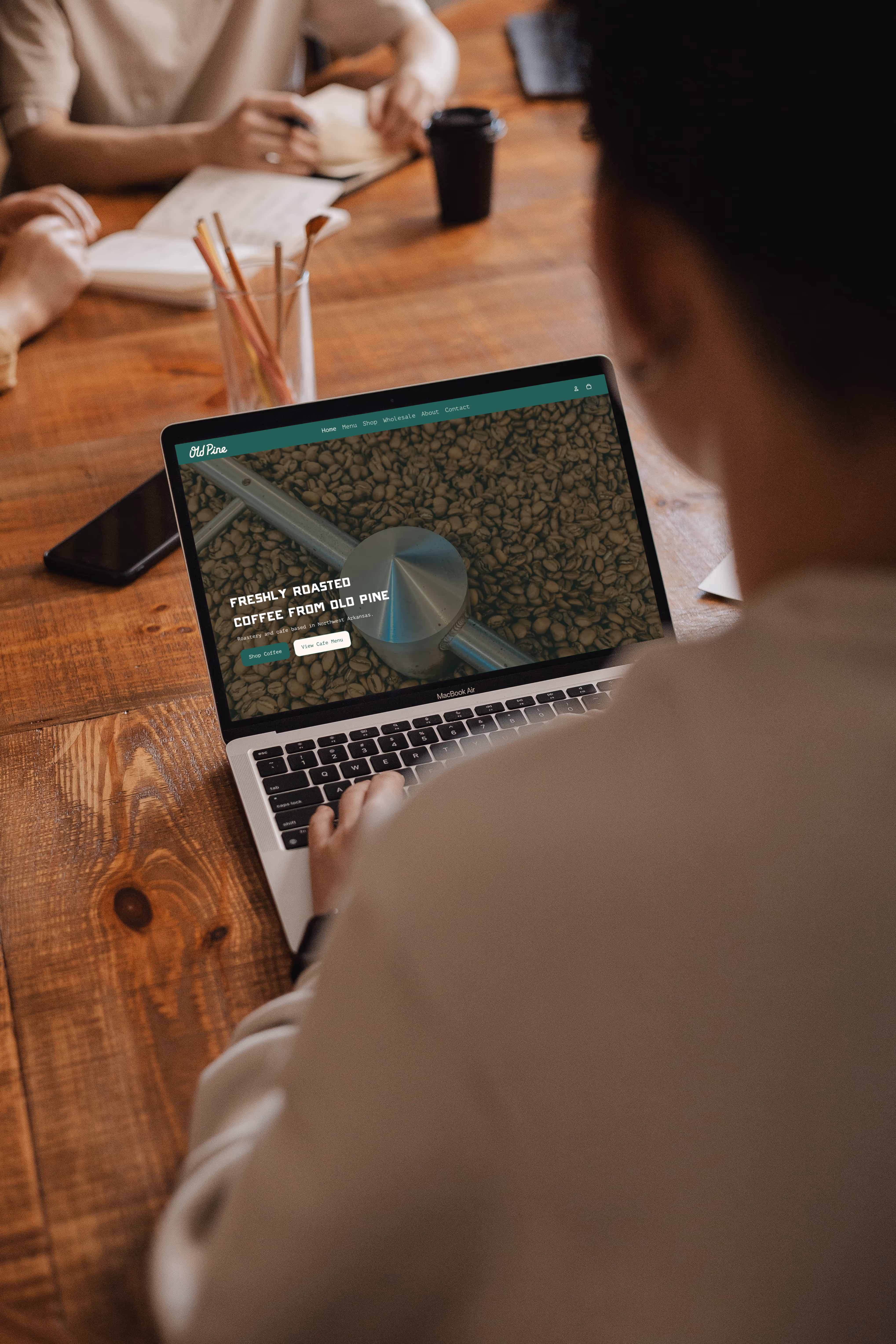 Person using a MacBook Air displaying a coffee website featuring roasted coffee beans and options to shop coffee or view cafe menu.