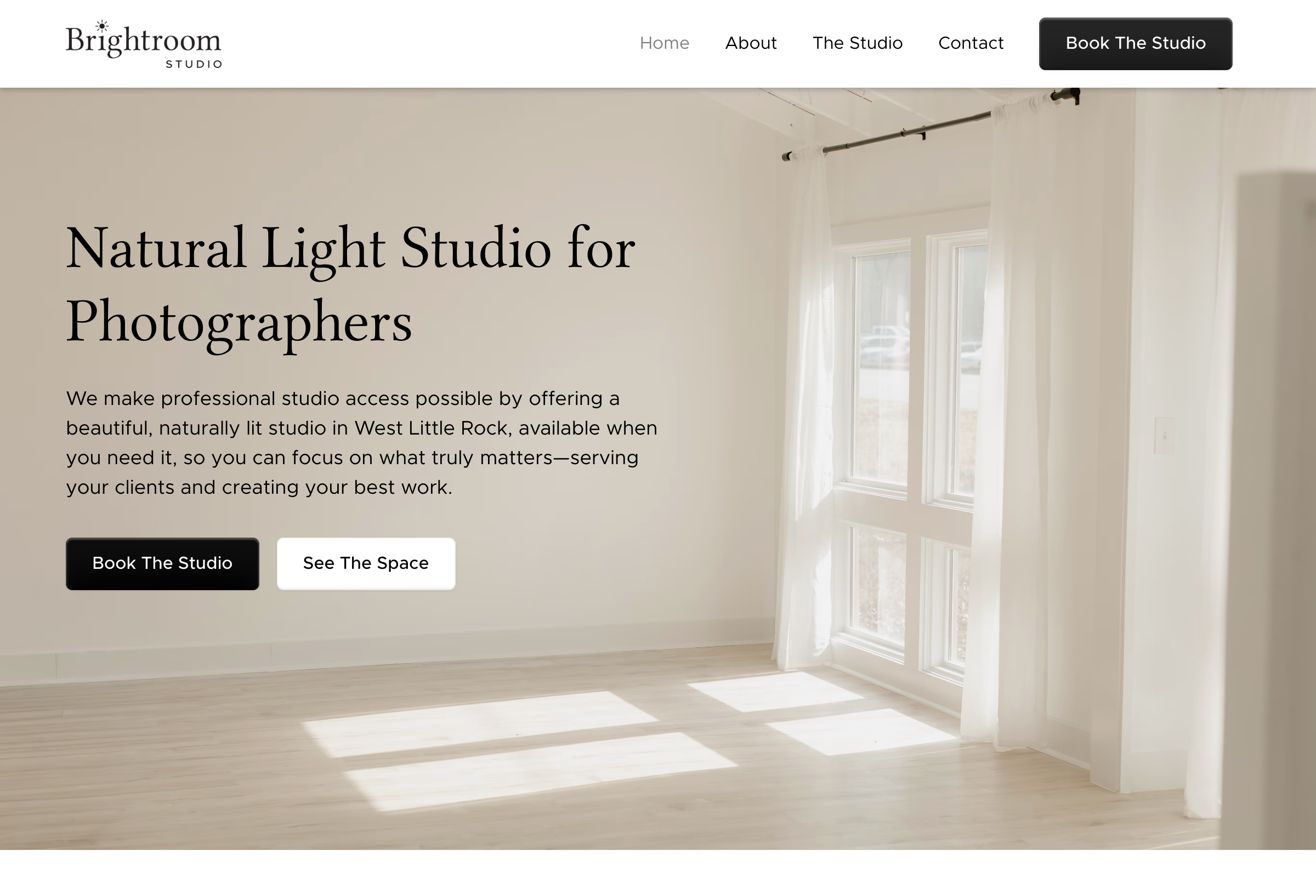 Bright, naturally lit photography studio space with large windows and sheer curtains casting sunlight on light wood floors.