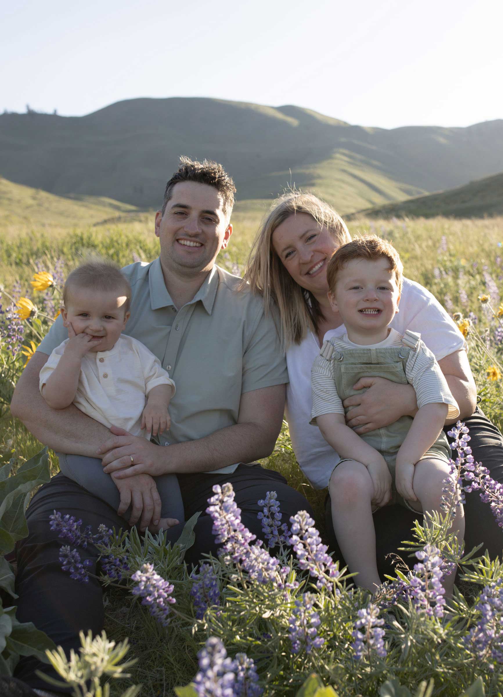 Photo of Dr. Michael's family. Smiling family of four sitting outdoors in a field of purple and yellow wildflowers with green hills in the background.