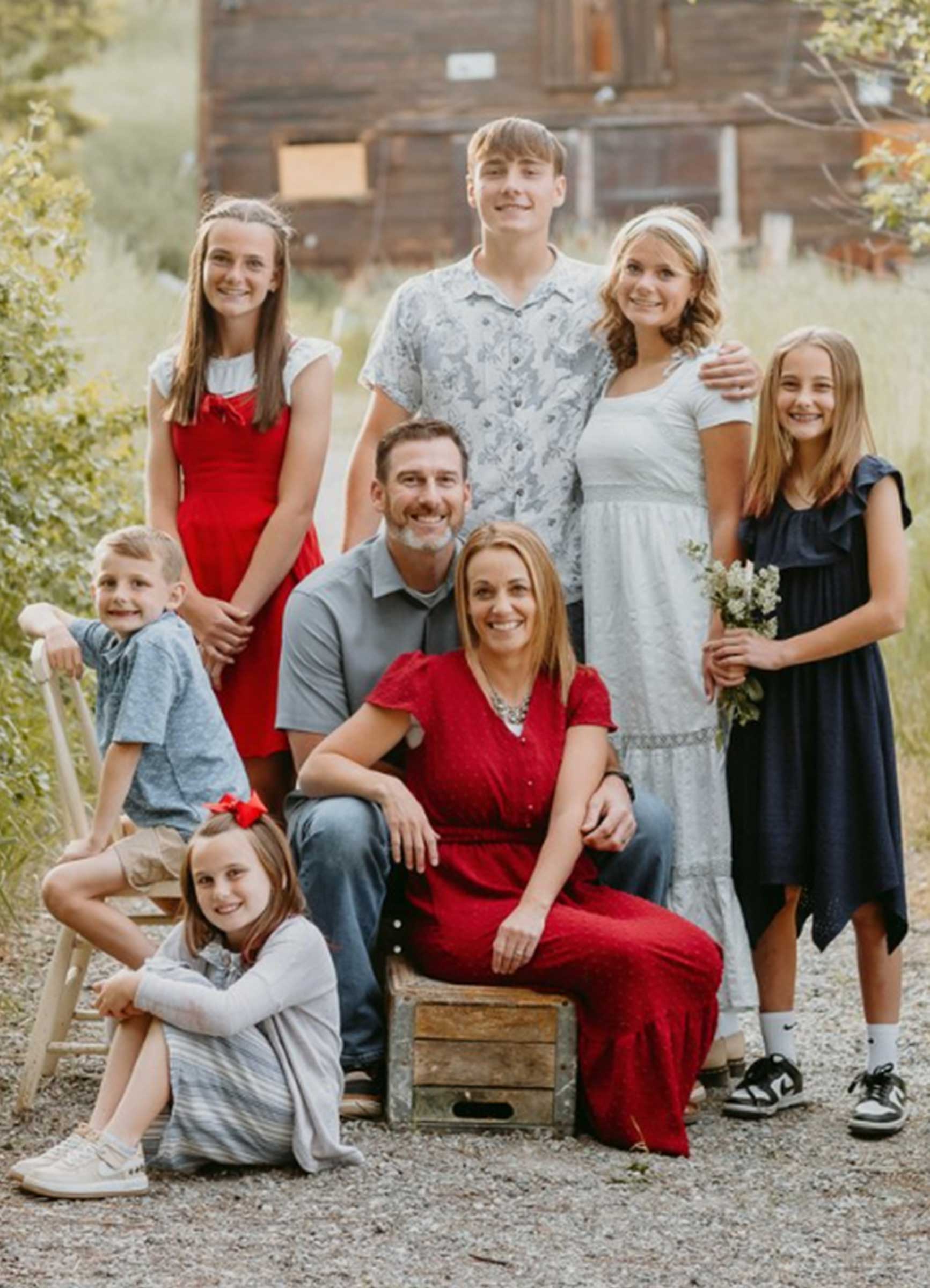 Family portrait Dr. Dickson's family. Eight people outdoors with a wooden building in the background, adults seated in front and children standing and sitting around them.