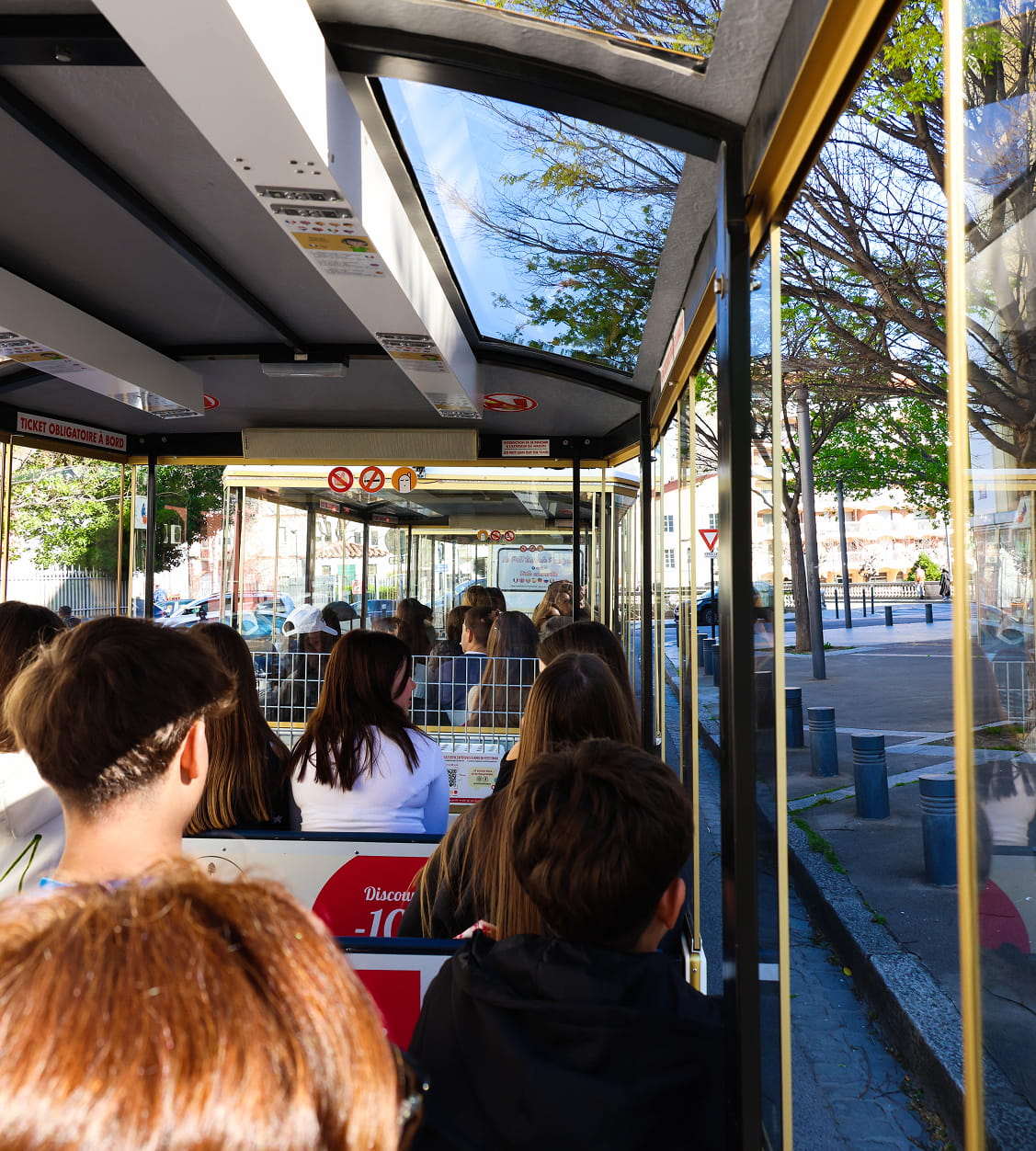 Intérieur d'un tramway ou d'un bus touristique avec plusieurs passagers assis, vu de l'arrière vers l'avant.