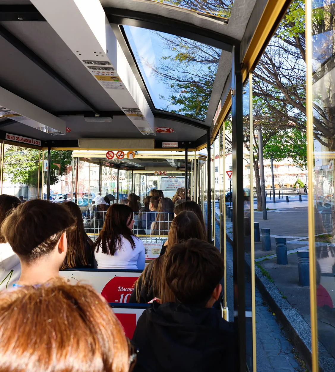 Intérieur d'un tramway ou d'un bus touristique avec plusieurs passagers assis, vu de l'arrière vers l'avant.