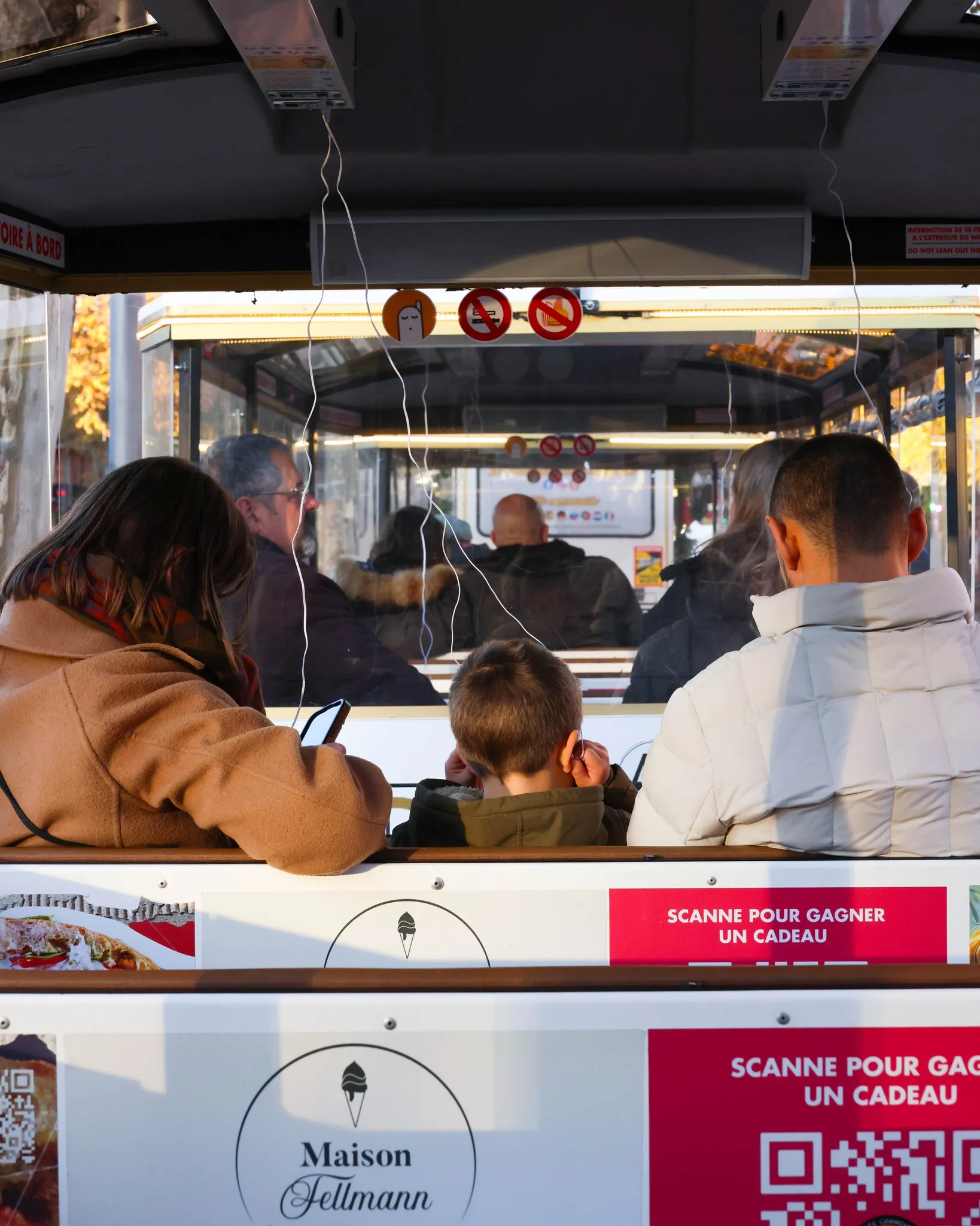 Des passagers assis de dos dans un tramway, avec des publicités pour Maison Fellmann sur les sièges.