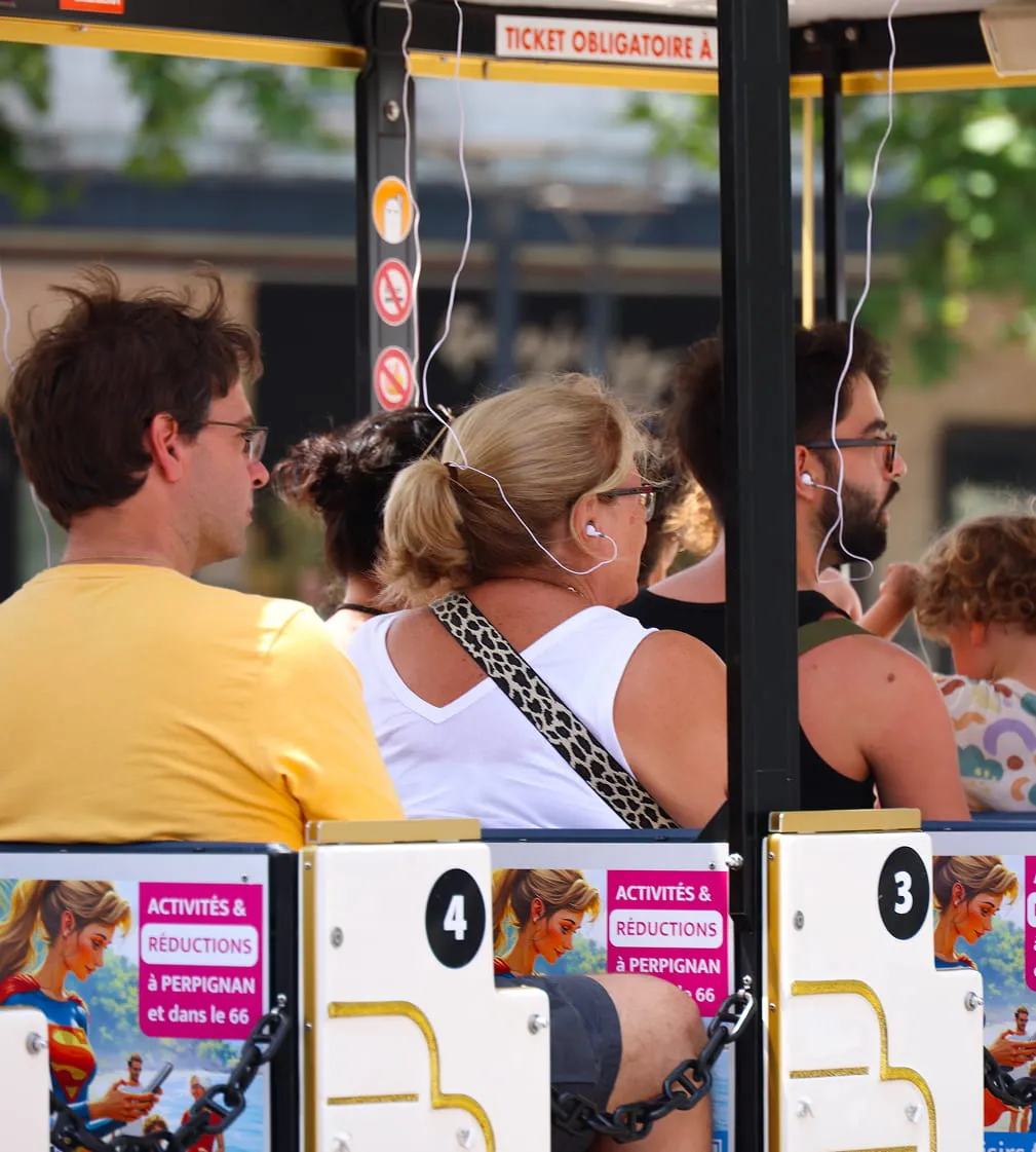 Groupe de personnes assises dans un petit train touristique en plein air, portant des écouteurs blancs, avec des affiches colorées sur les dossiers des sièges.